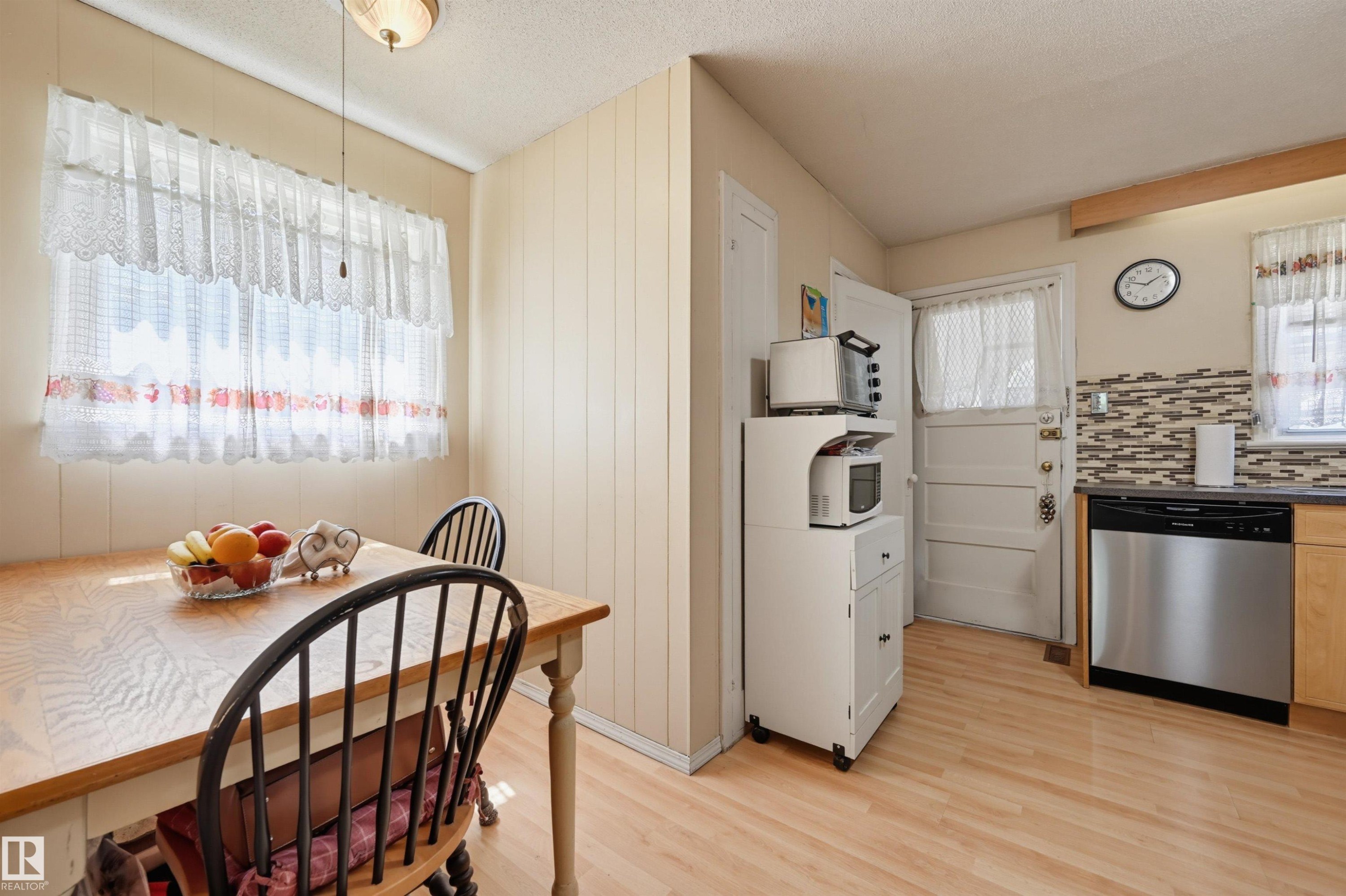 Kitchen with wood-finish flooring, a mosaic tile backsplash, and a stainless steel dishwasher - 11414 88 Street Nw, Edmonton, AB