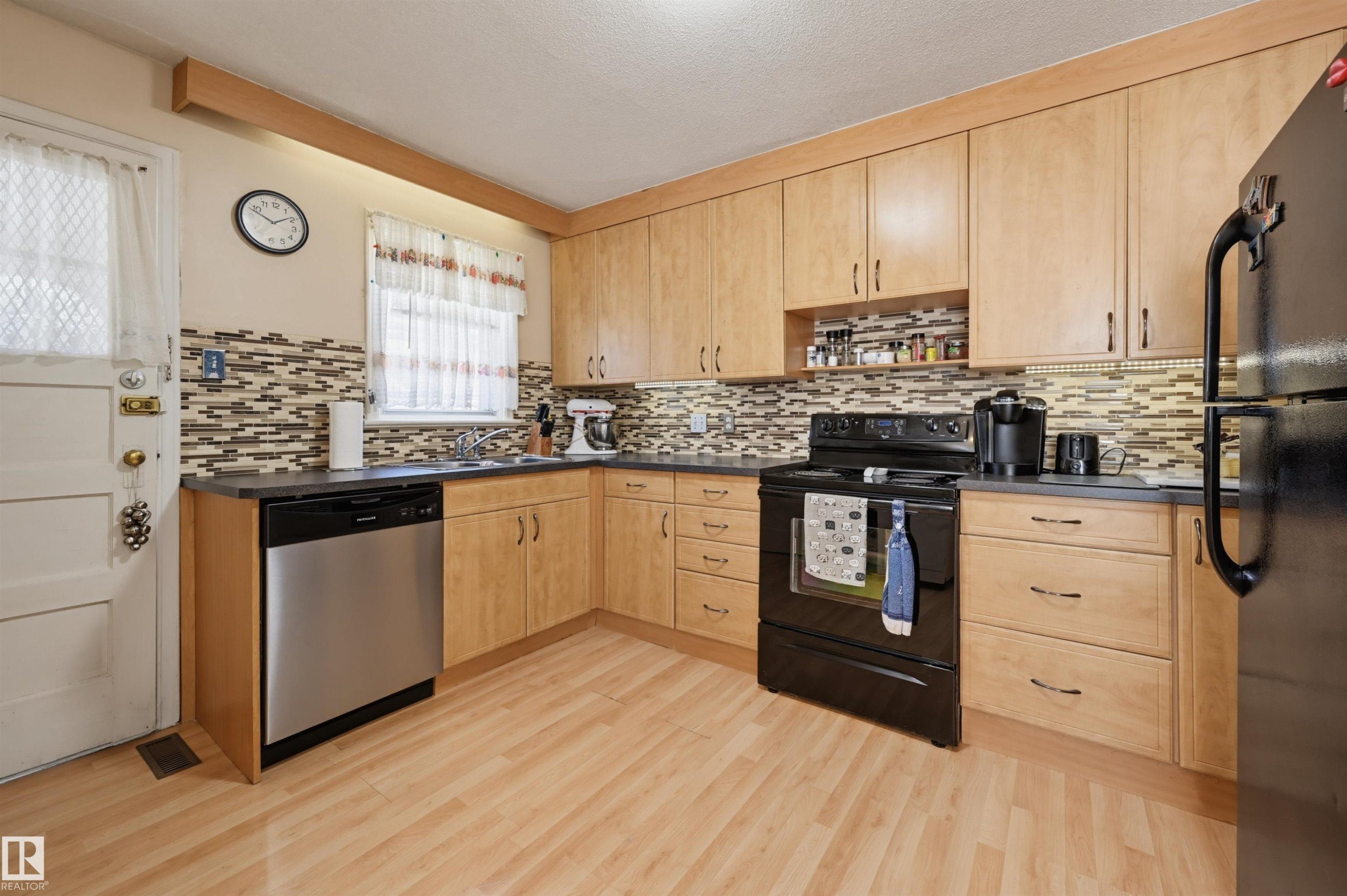Kitchen featuring light wood-finish cabinetry, dark countertops, and a mosaic tile backsplash - 11414 88 Street Nw, Edmonton, AB