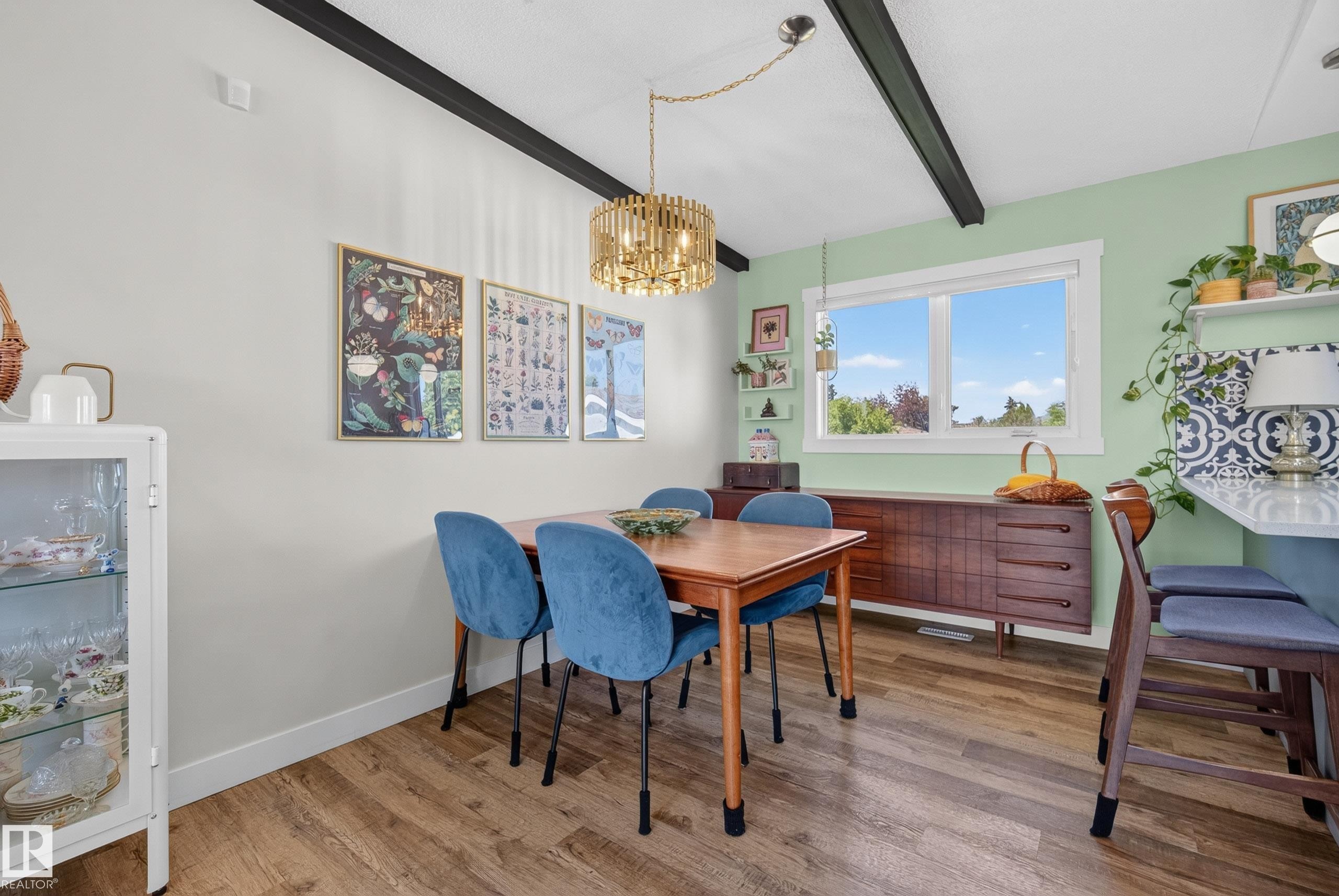 Dining space featuring wood-finish flooring, exposed ceiling beams, and a modern gold-tone chandelier - 14128 73 Street, Edmonton, AB
