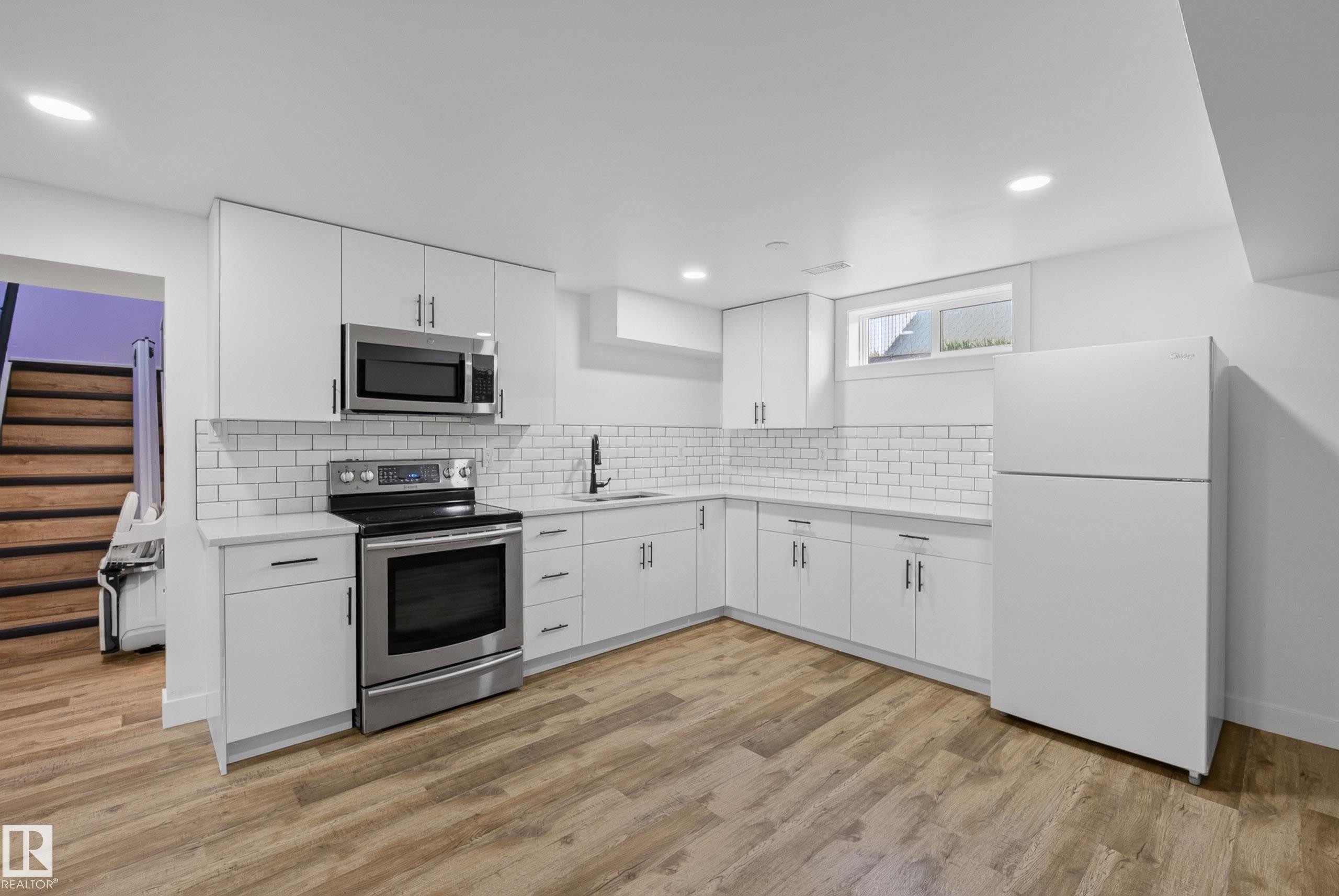 Modern kitchen featuring white cabinetry, subway tile backsplash, stainless steel appliances, and wood-finish flooring - 14128 73 Street, Edmonton, AB