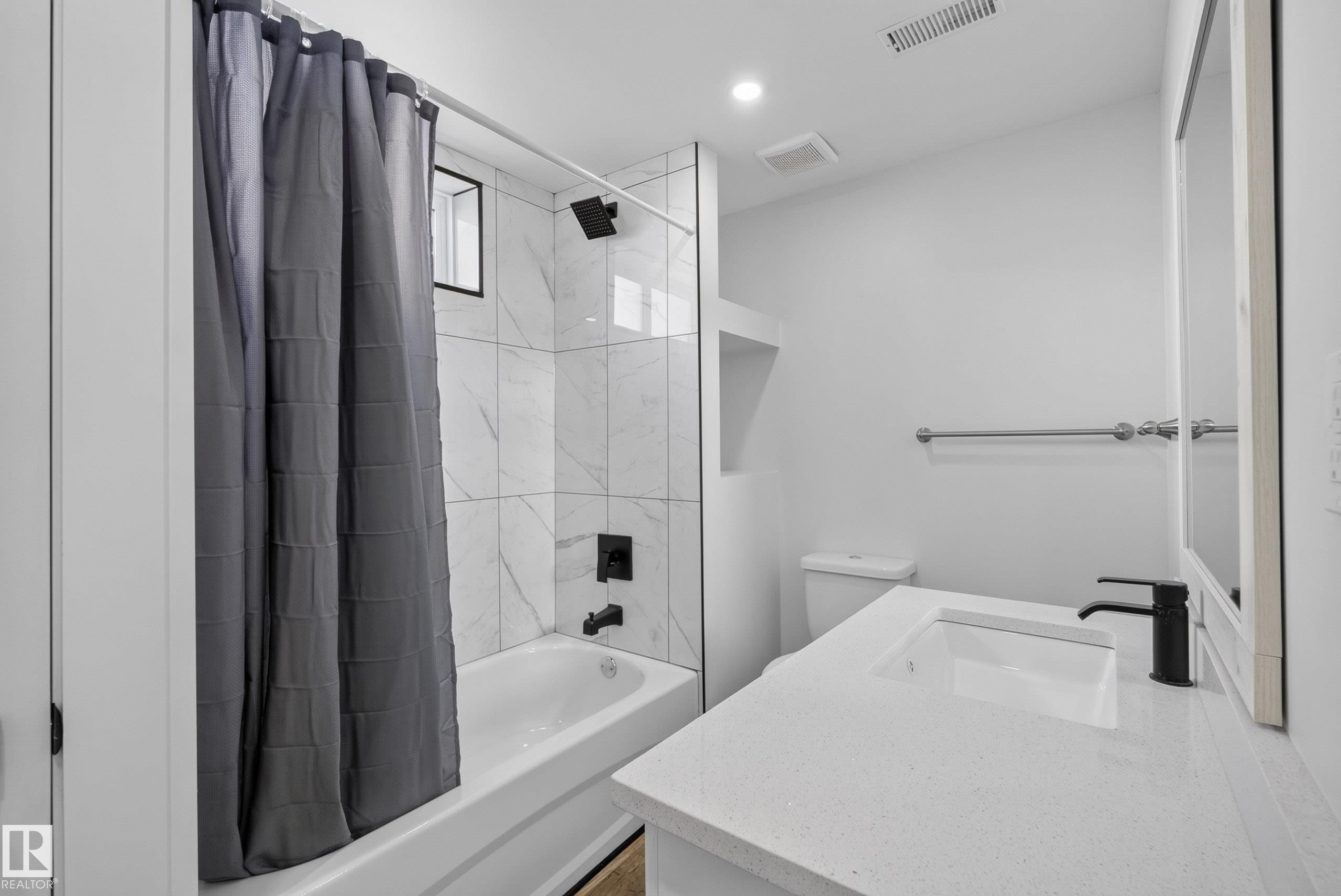 Modern bathroom featuring a white vanity with an integrated sink, black single-handle faucet, and white countertop - 14128 73 Street, Edmonton, AB
