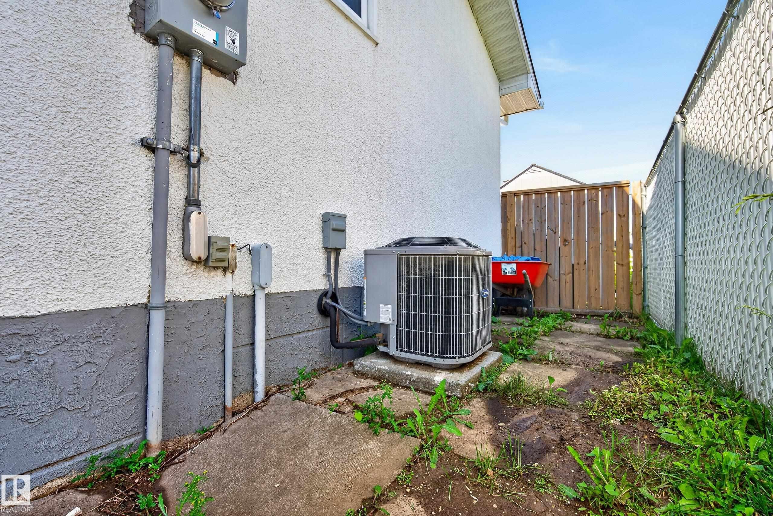Exterior stucco siding with a painted foundation, featuring an outdoor HVAC unit on a concrete pad - 14128 73 Street, Edmonton, AB