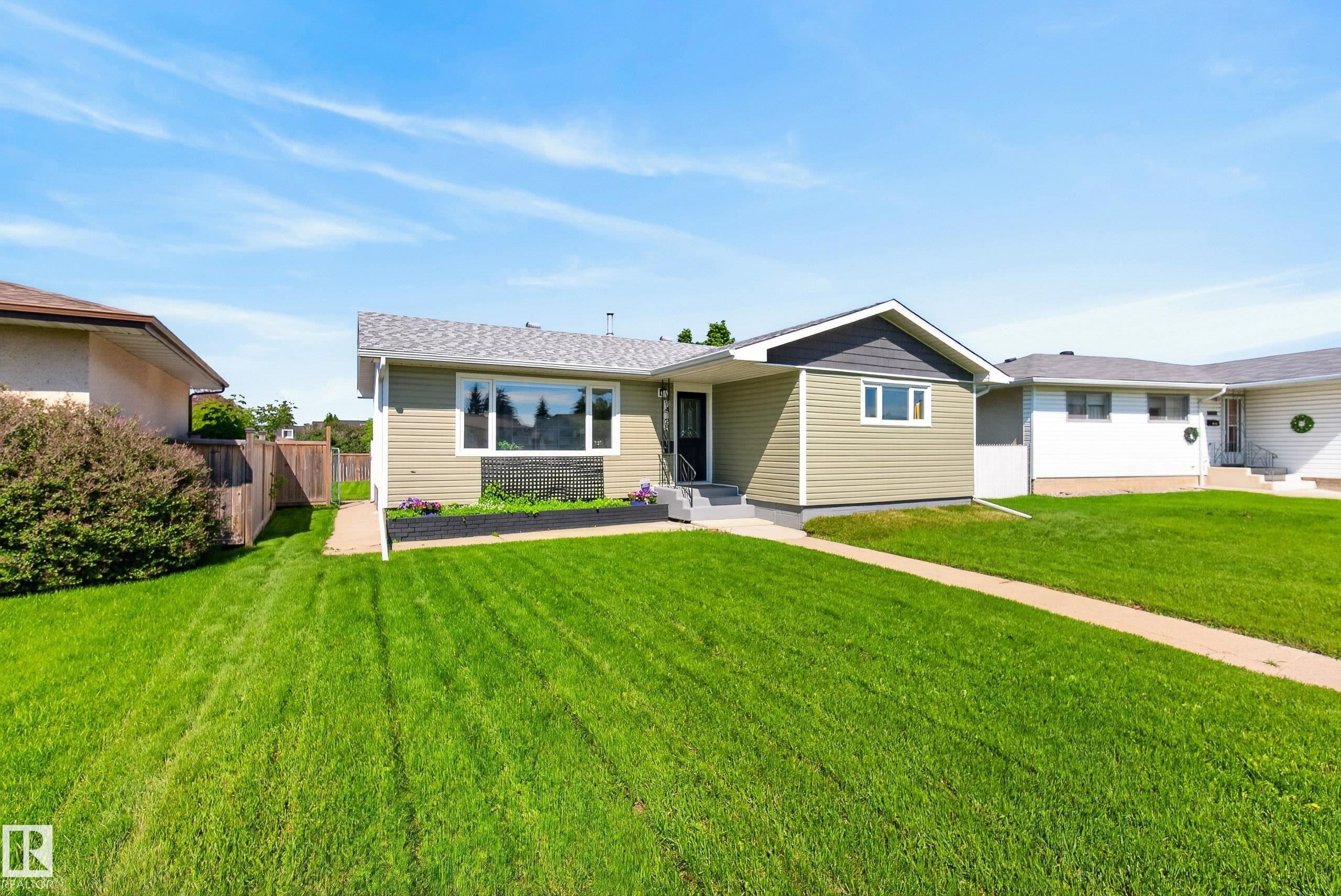 Ranch-style exterior featuring light green siding, a contrasting dark gray gable, a dark asphalt shingle roof, and a black front door - 14128 73 Street, Edmonton, AB