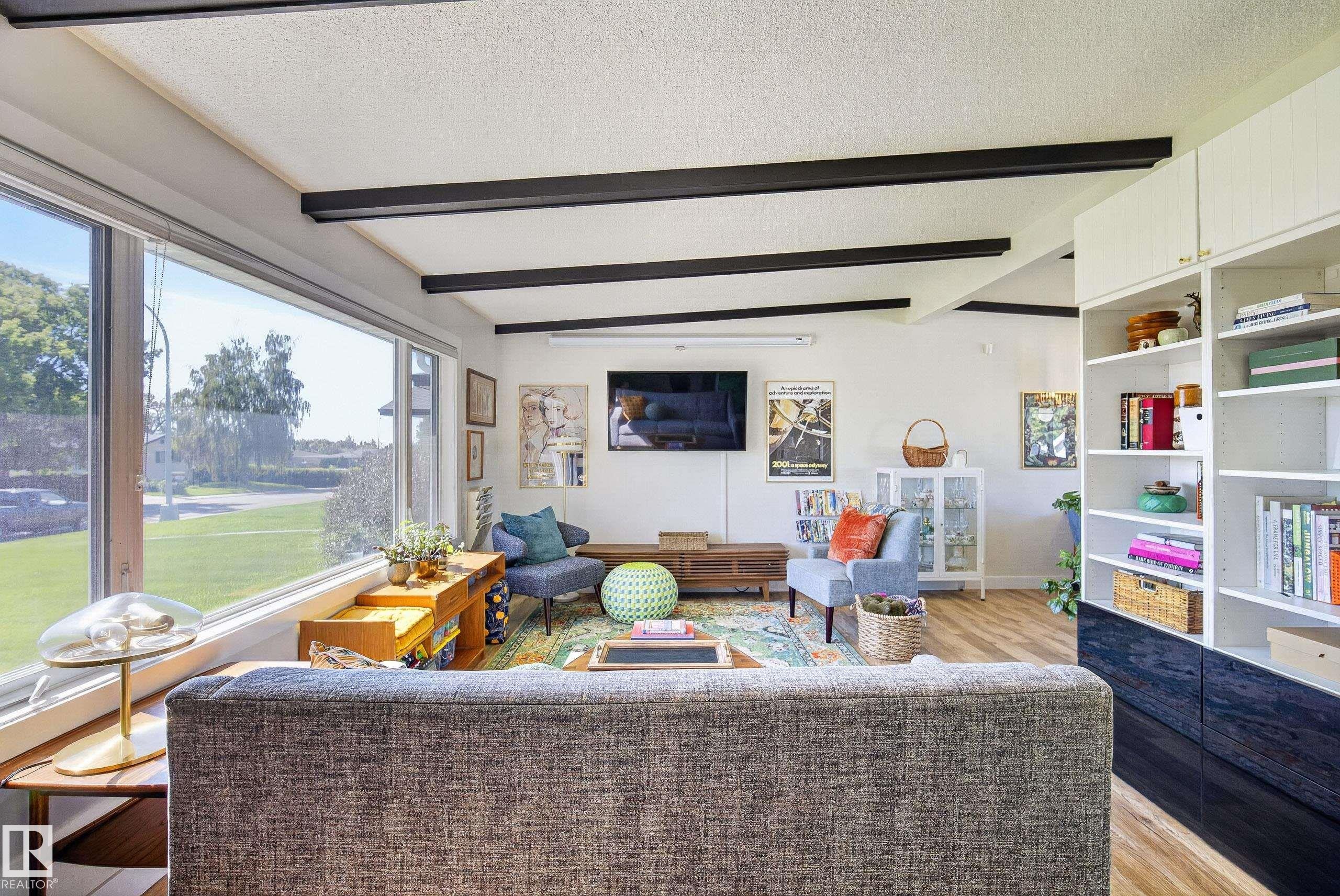 Spacious living area featuring expansive windows, exposed ceiling beams, built-in shelving, and wood-finish flooring - 14128 73 Street, Edmonton, AB