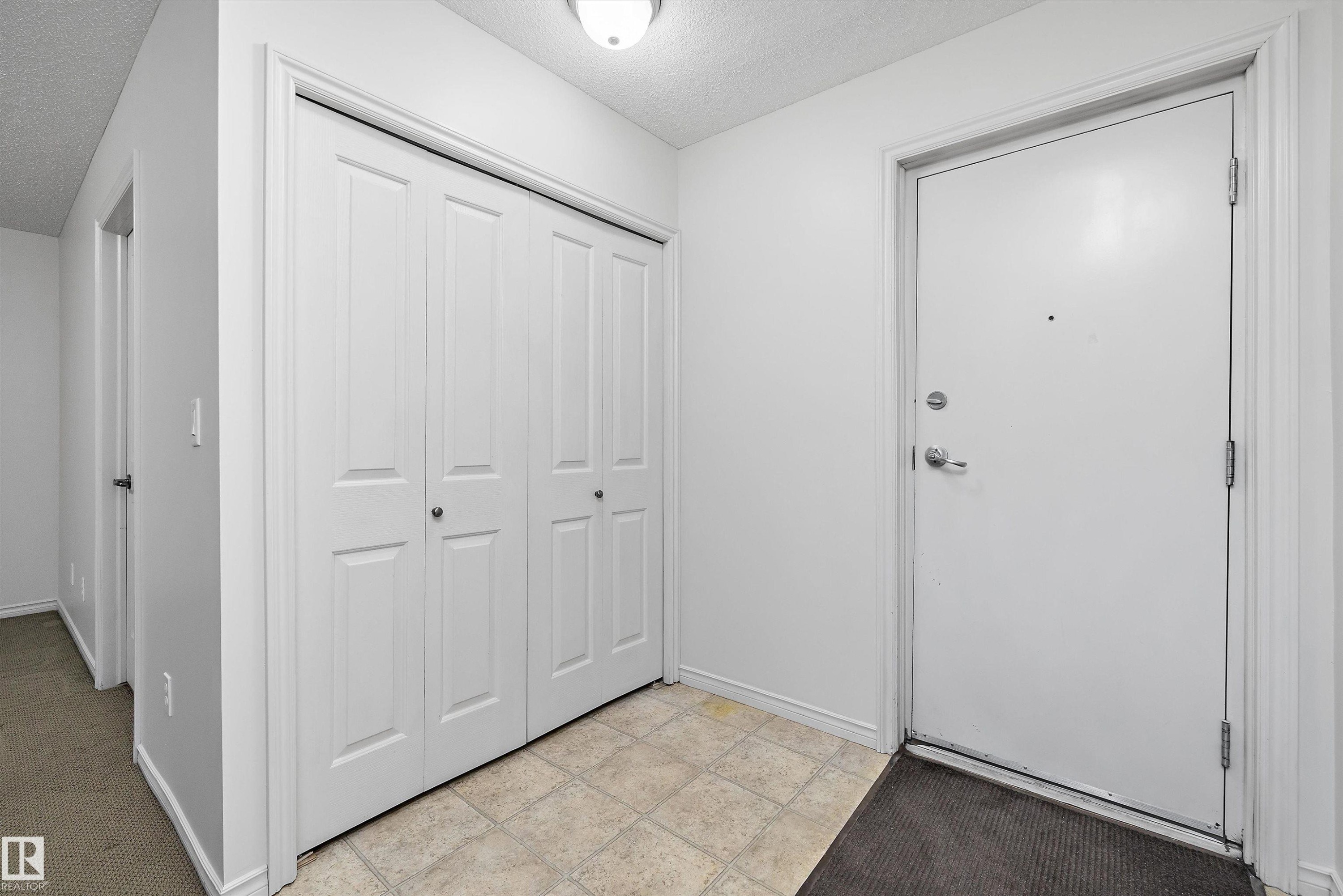 Entryway featuring a solid white door with chrome hardware, an overhead flush-mount light fixture, and a spacious bi-fold closet with paneled doors - 101 13825 155 Avenue, Edmonton, AB