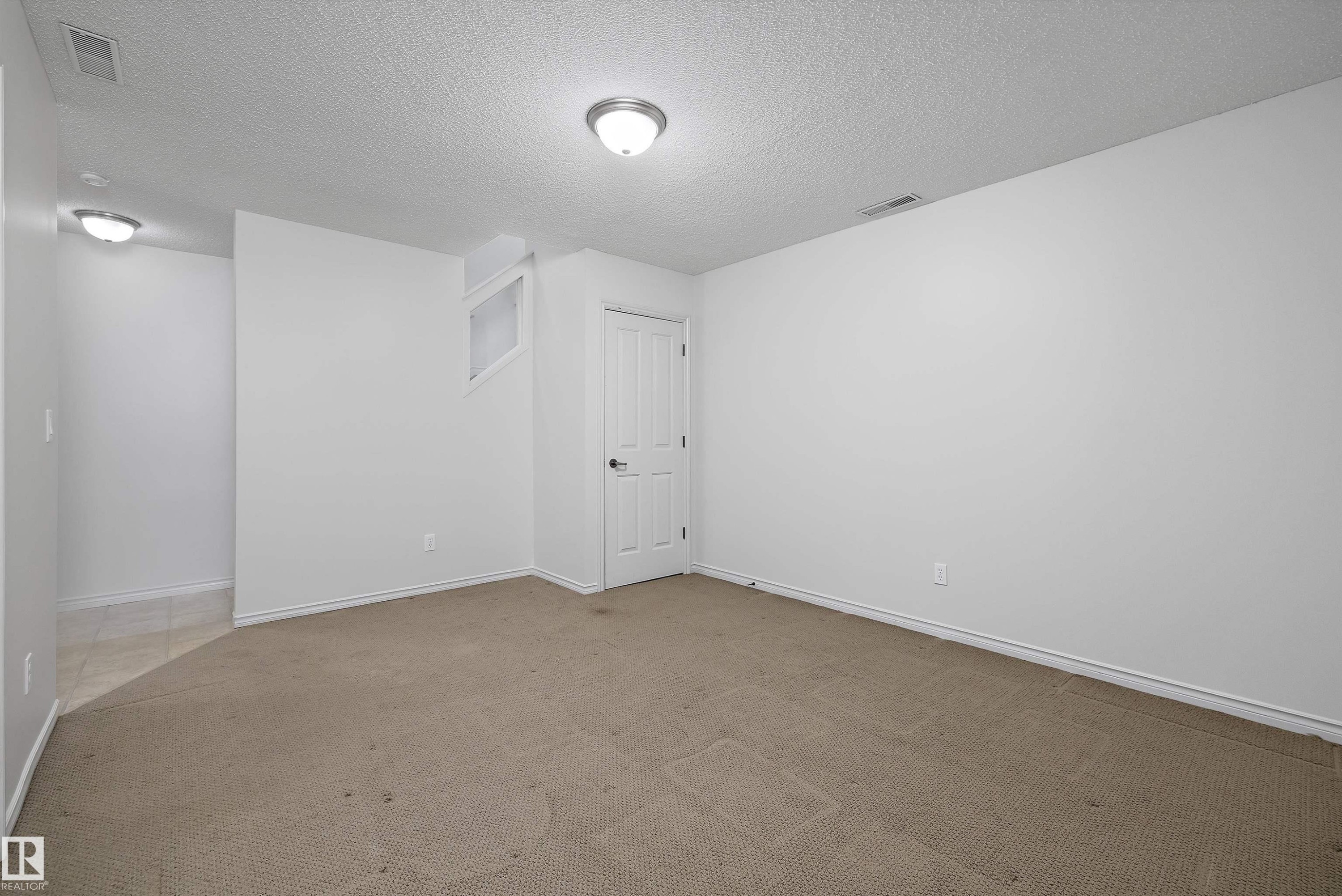 Spacious room with neutral carpeting, white walls, and a textured ceiling - 101 13825 155 Avenue, Edmonton, AB