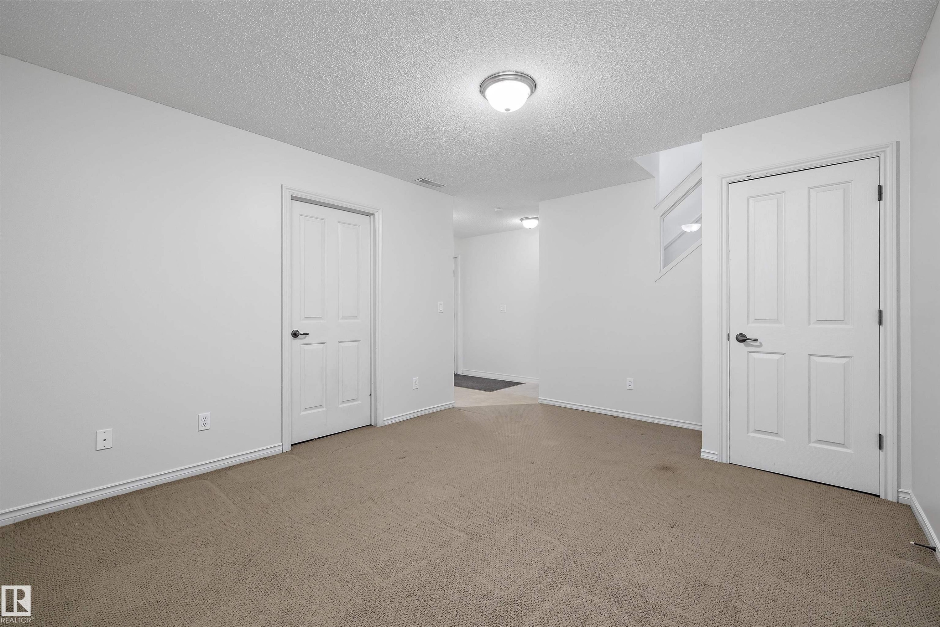 Versatile room featuring two paneled doors, neutral carpeting, and white walls - 101 13825 155 Avenue, Edmonton, AB