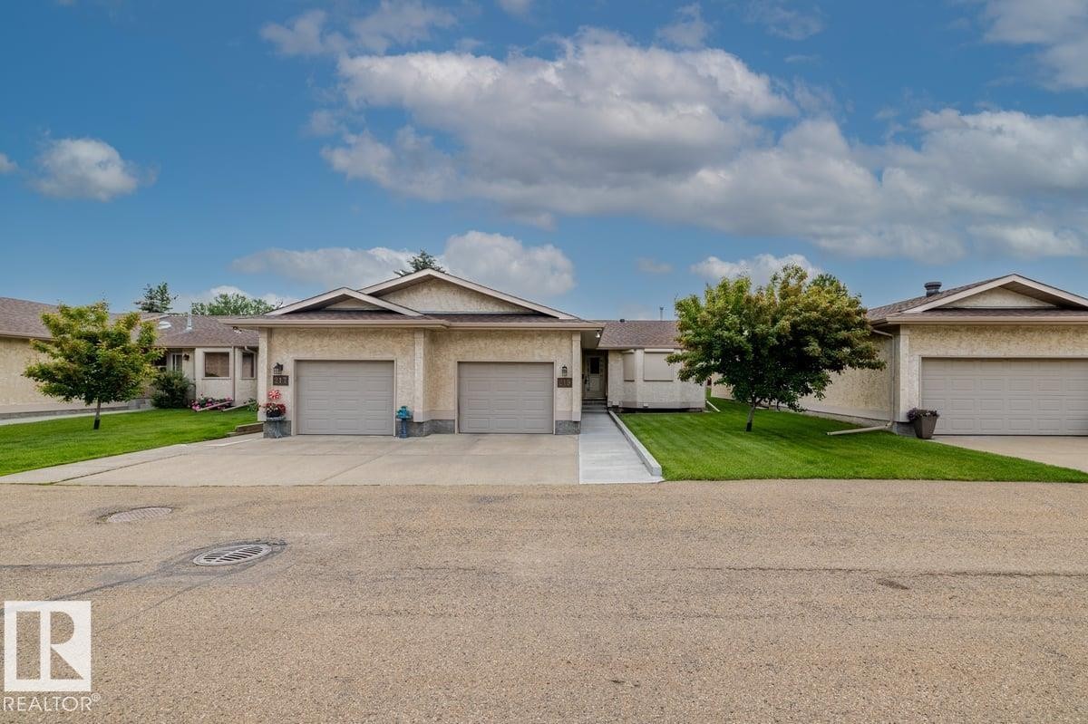 Ranch-style property featuring a stucco exterior, attached two-car garage, concrete driveway, and a manicured lawn with established trees - 219 Knottwood Road, Edmonton, AB