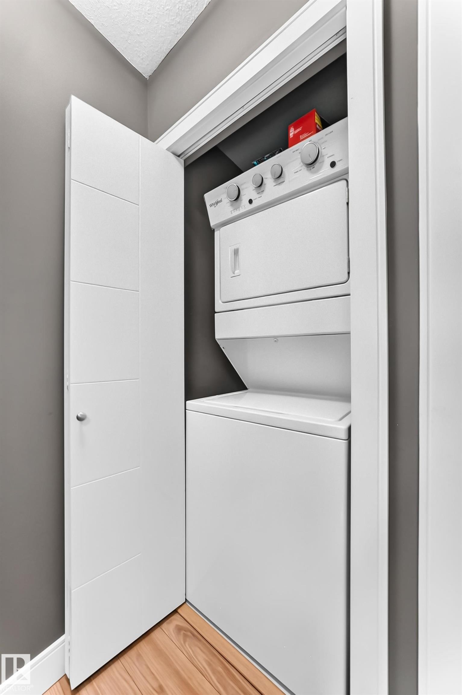 Stackable laundry appliances within a dedicated closet space, featuring wood-finish flooring and modern white doors - 37 13003 132 Avenue Nw, Edmonton, AB