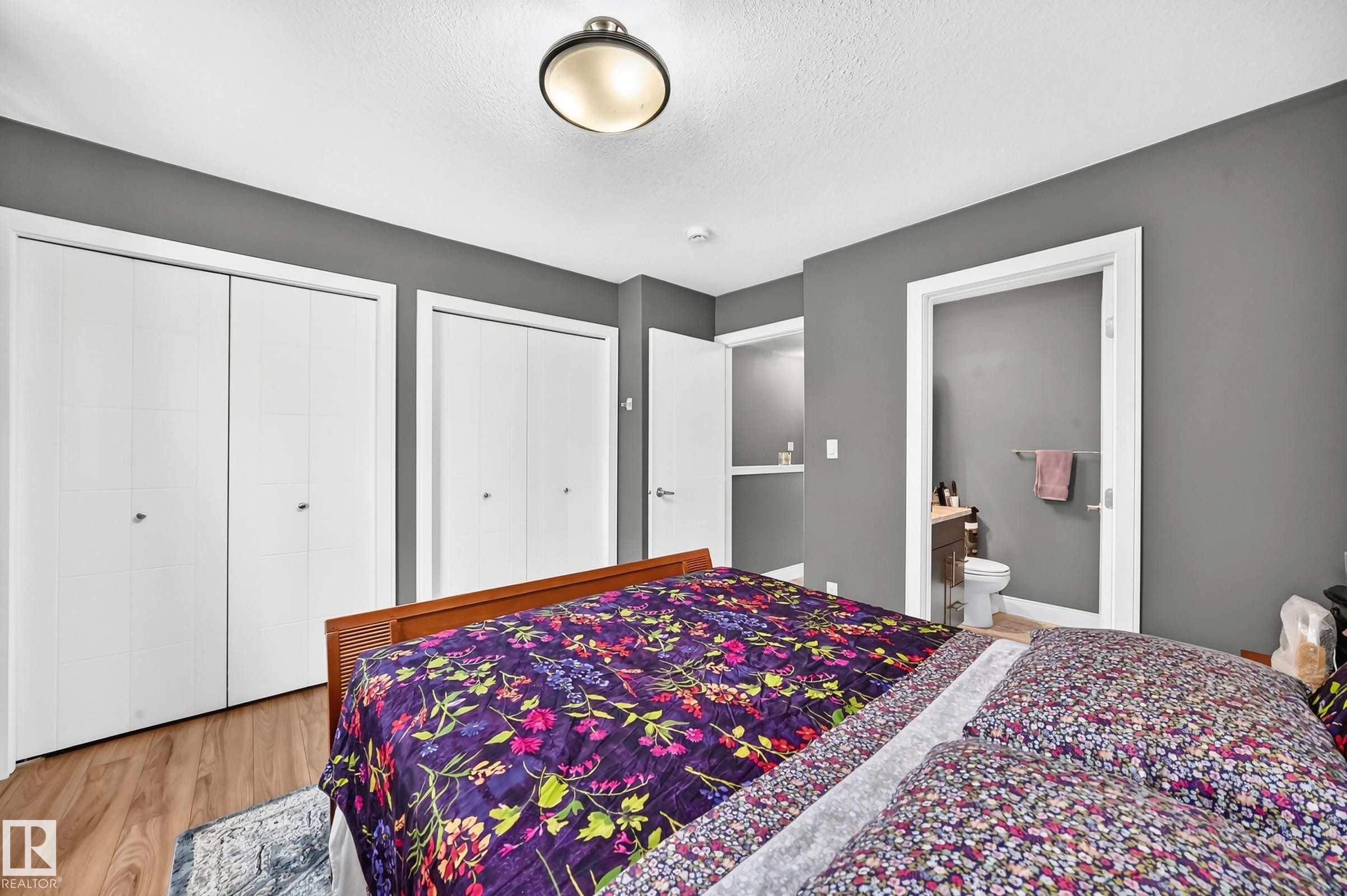 Bedroom featuring wood-finish flooring, two sets of bi-fold closet doors, and recessed shelving - 37 13003 132 Avenue Nw, Edmonton, AB
