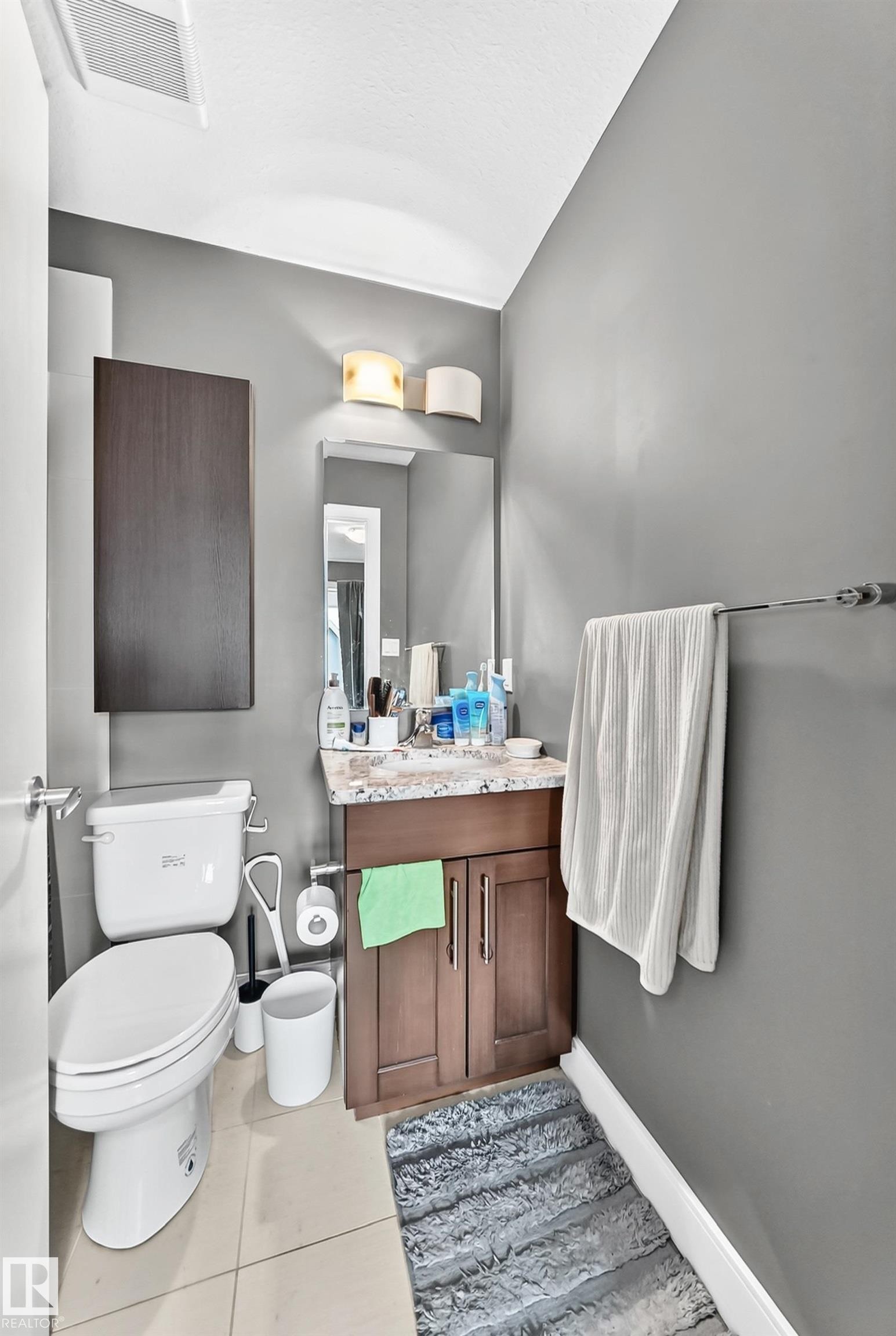 Bathroom featuring a wood-finish vanity with a stone countertop, an undermount sink, and a wall-mounted mirror - 37 13003 132 Avenue Nw, Edmonton, AB