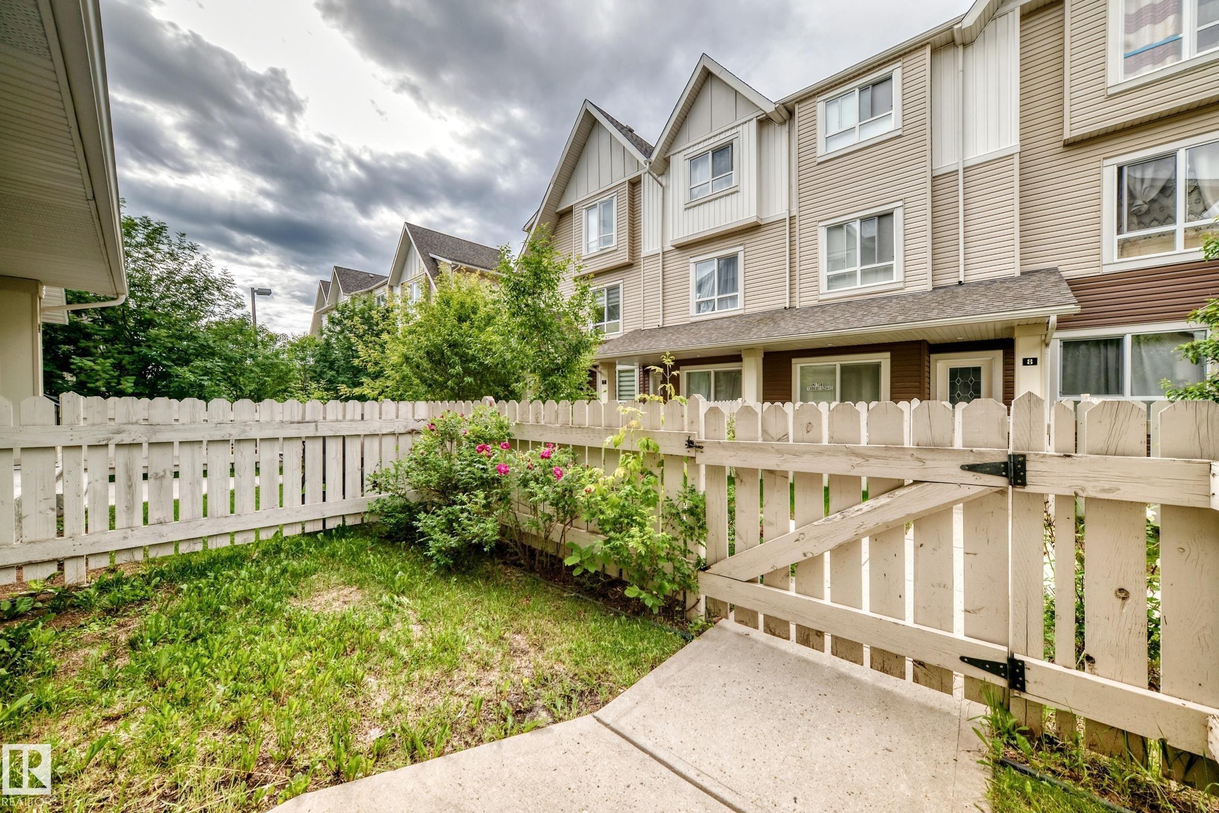 White picket fence enclosing a compact green space with established shrubbery and floral accents - 37 13003 132 Avenue Nw, Edmonton, AB