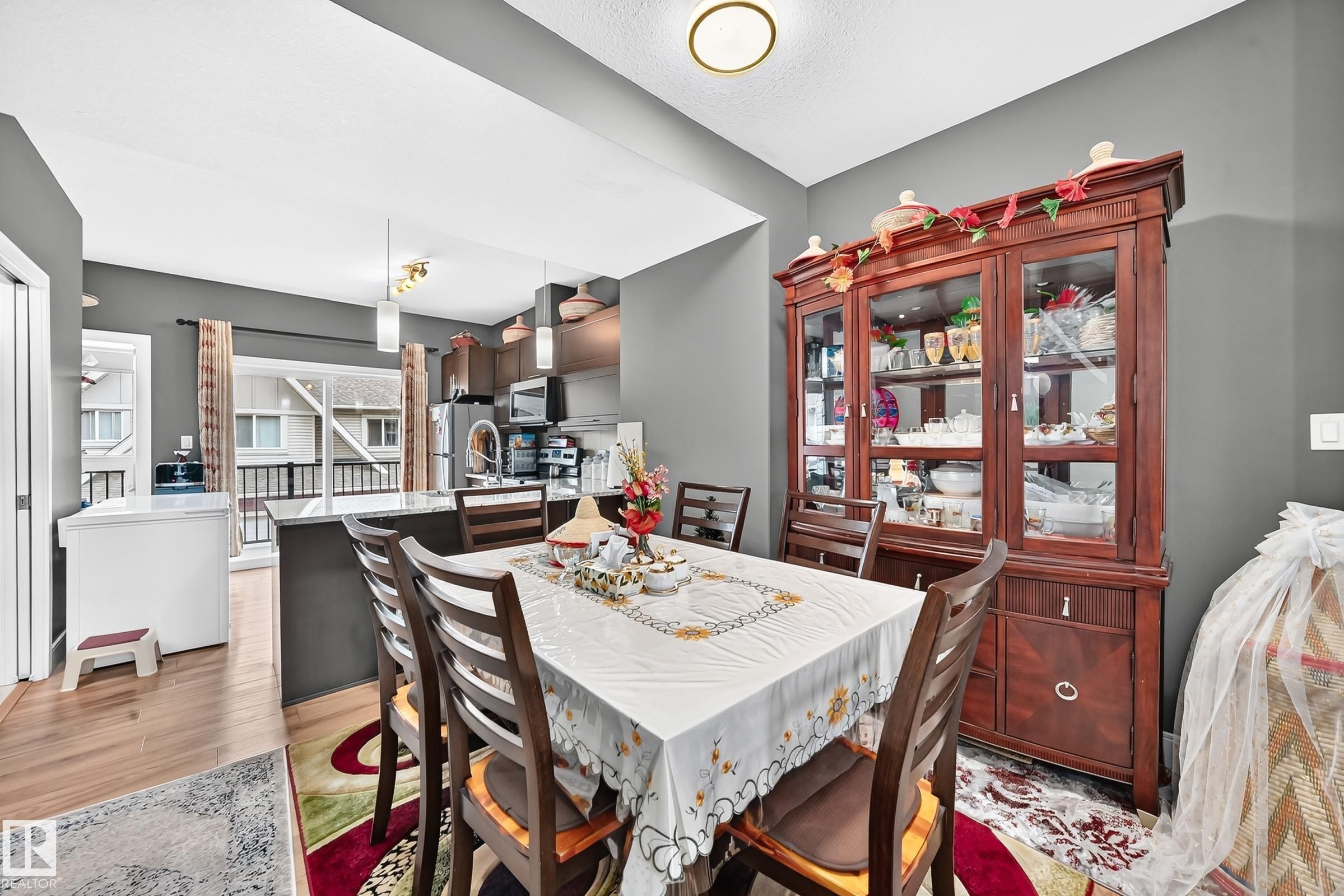 Dining area featuring wood-finish flooring, a contemporary ceiling light fixture, a sliding glass door leading to an exterior balcony, and a kitchen island with pendant lighting - 37 13003 132 Avenue Nw, Edmonton, AB
