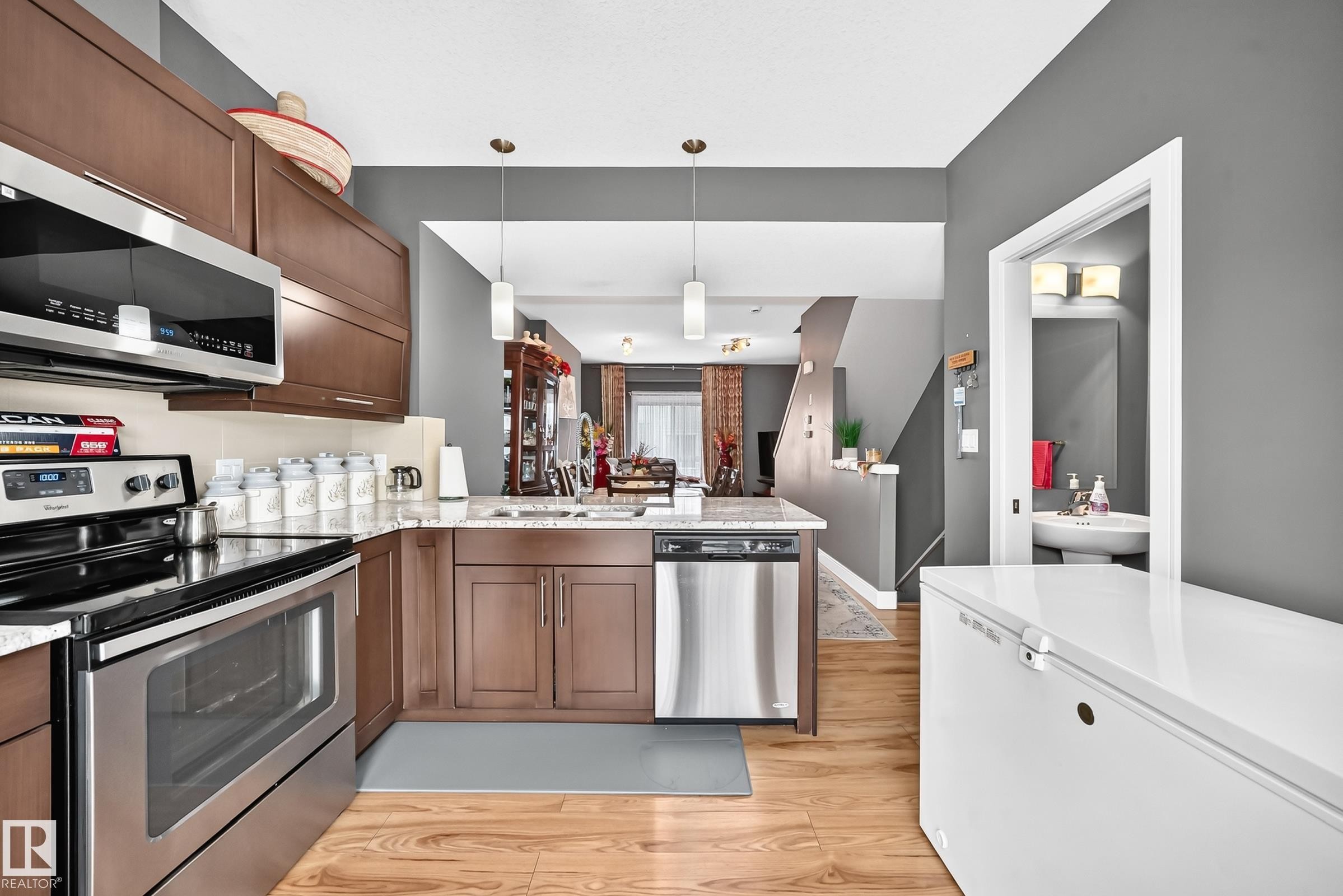 Kitchen featuring wood-finish flooring, stainless steel appliances, pendant lighting, shaker-style cabinetry, and a light-toned countertop - 37 13003 132 Avenue Nw, Edmonton, AB