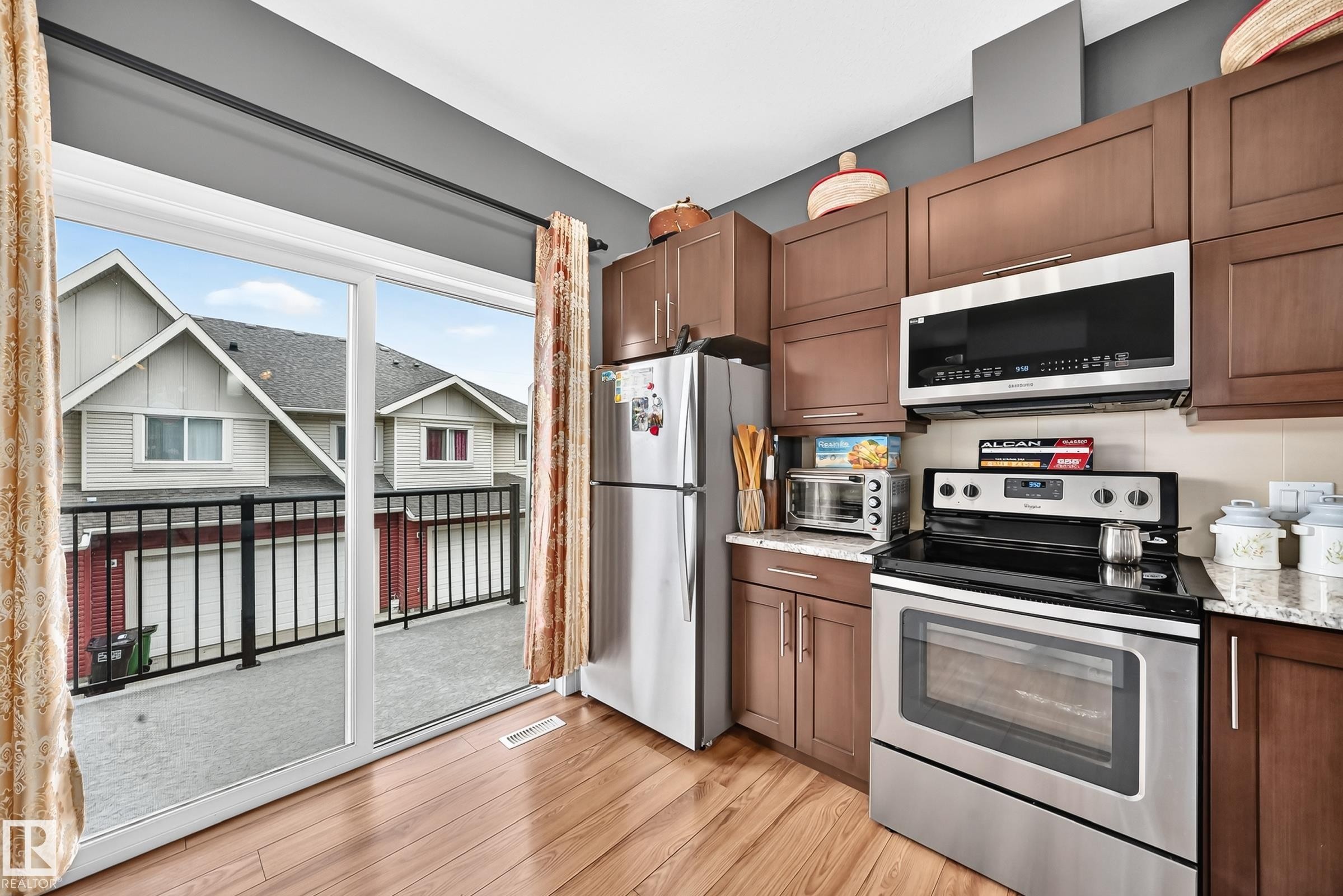 Kitchen featuring wood-finish flooring, dark wood cabinetry, and stainless steel appliances - 37 13003 132 Avenue Nw, Edmonton, AB