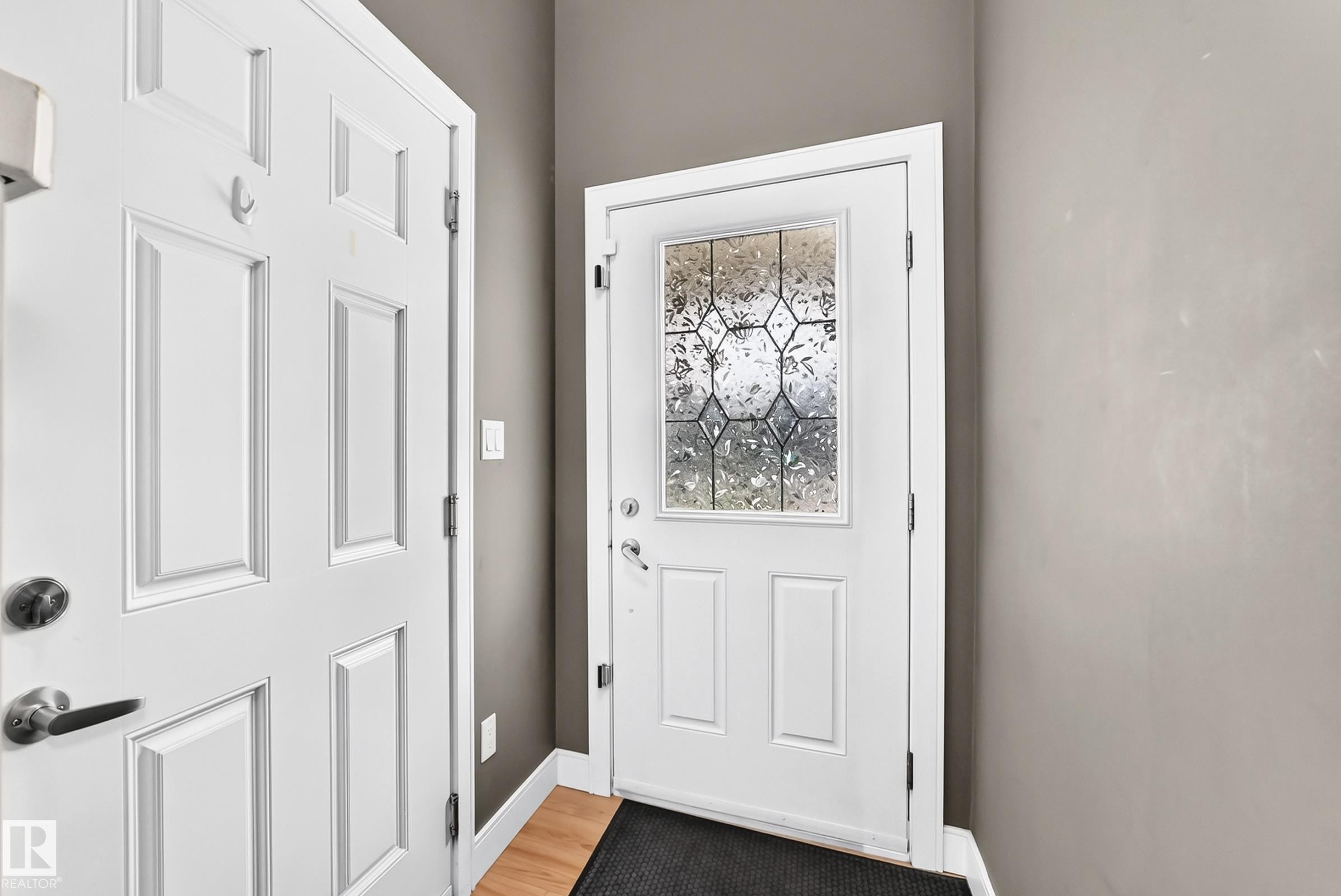 Entryway featuring a white paneled door with decorative leaded glass, wood-finish flooring, and neutral wall paint - 37 13003 132 Avenue Nw, Edmonton, AB