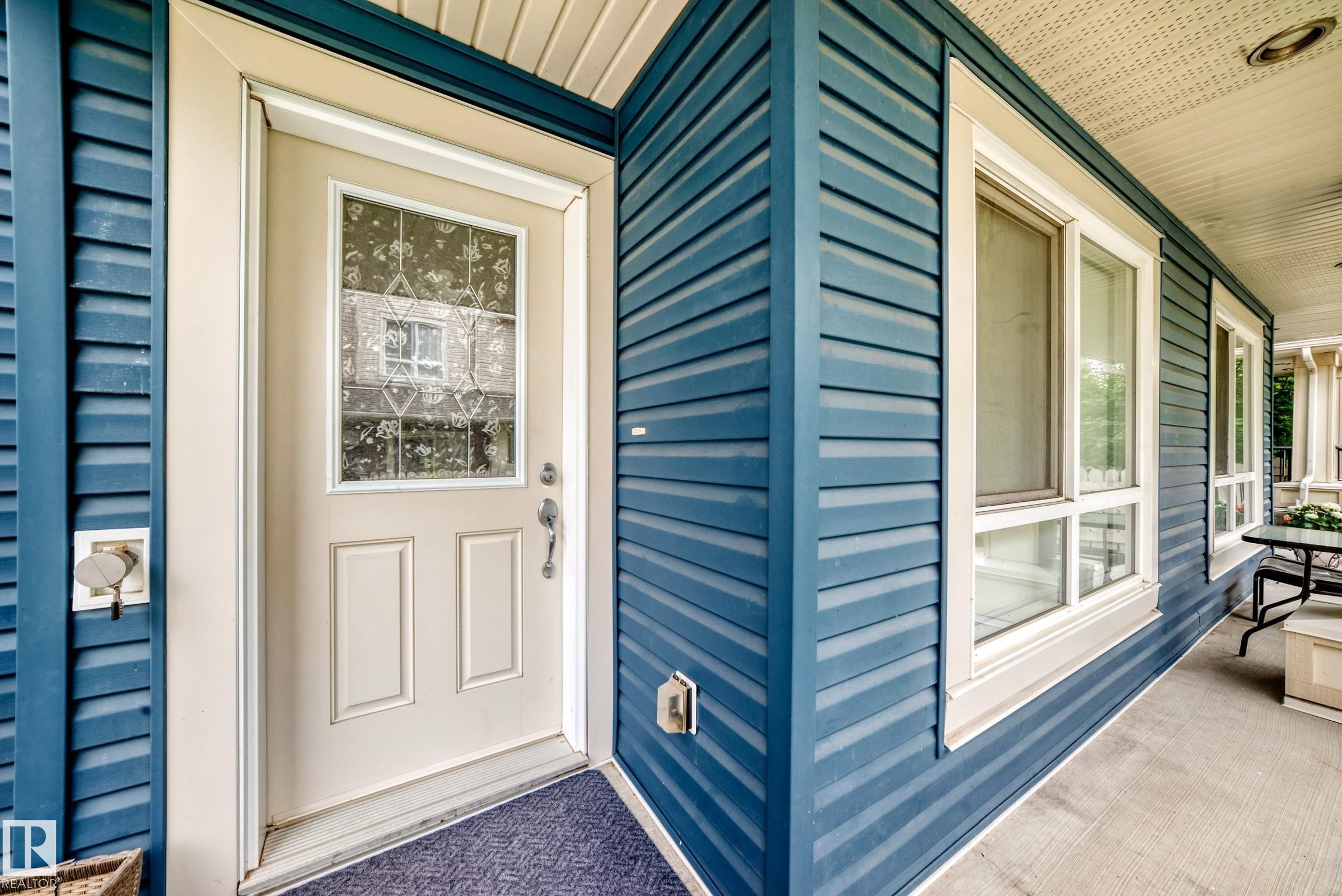 Entryway featuring a decorative glass panel door, blue horizontal siding, white trim, and a covered porch with concrete flooring - 37 13003 132 Avenue Nw, Edmonton, AB