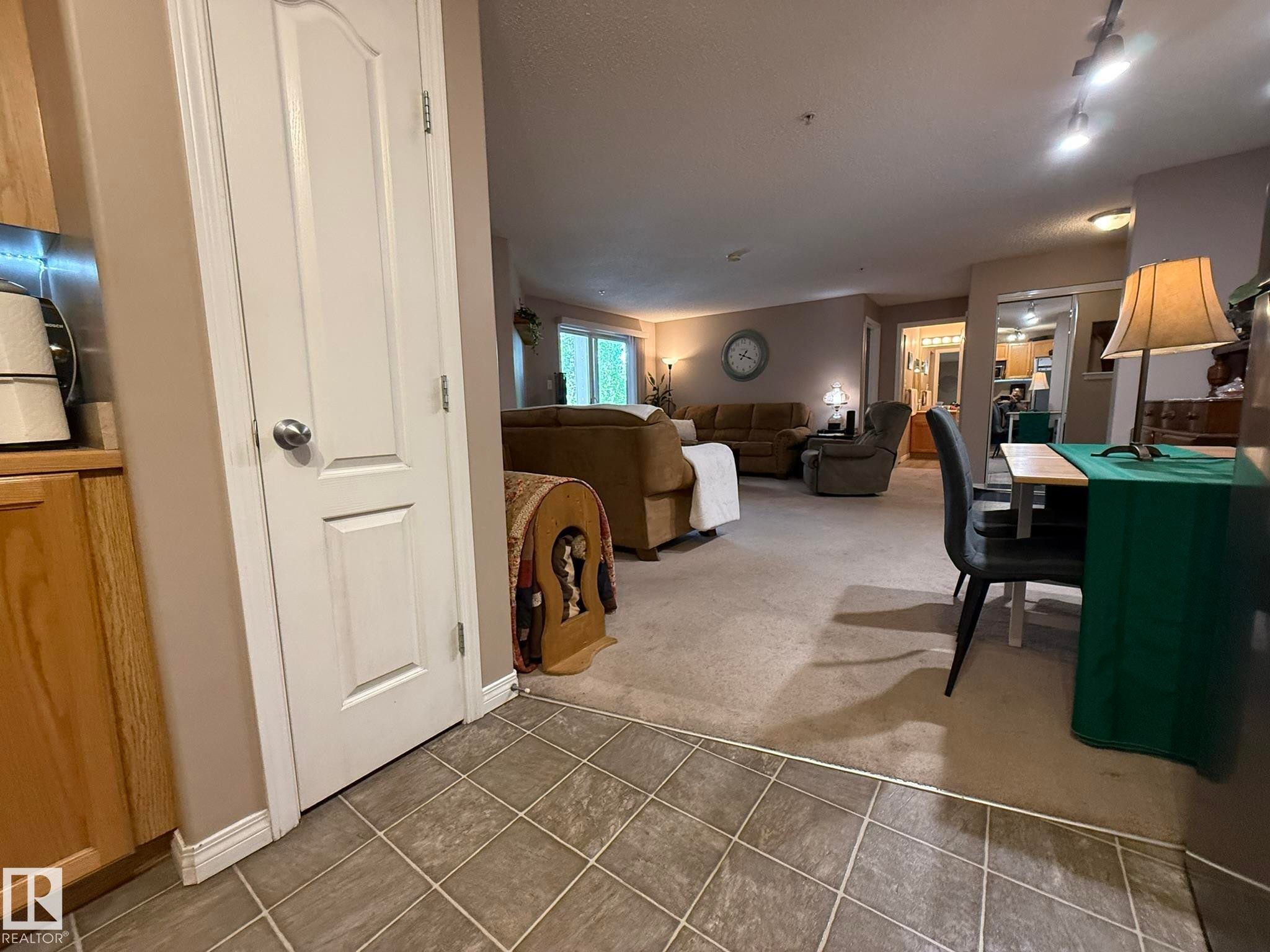 Entryway featuring tile flooring transitioning to carpeted living areas, wood-finish cabinetry, and interior paneled doors - 205 3425 19 Street, Edmonton, AB