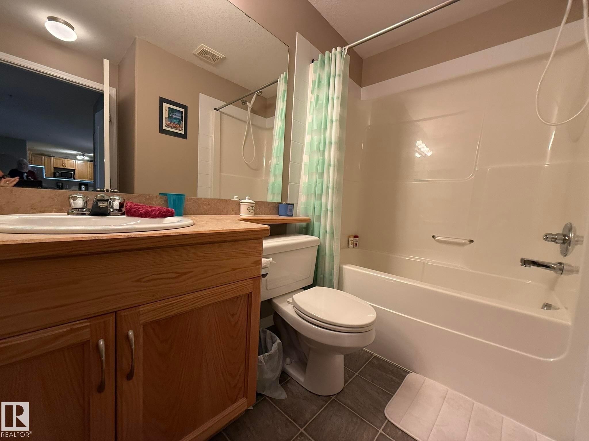 Bathroom featuring a wood-finish vanity with a built-in sink, a full-width mirror, and a toilet - 205 3425 19 Street, Edmonton, AB
