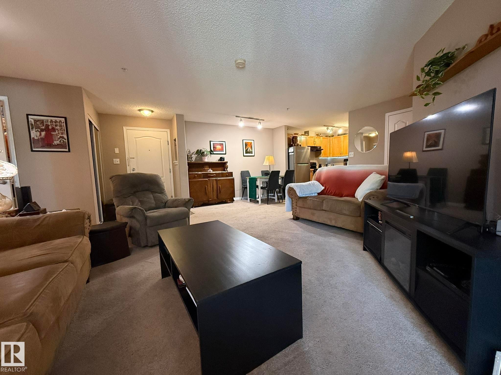 Open-concept living area featuring neutral carpet flooring, recessed lighting, and a kitchen with wood-finish cabinetry - 205 3425 19 Street, Edmonton, AB