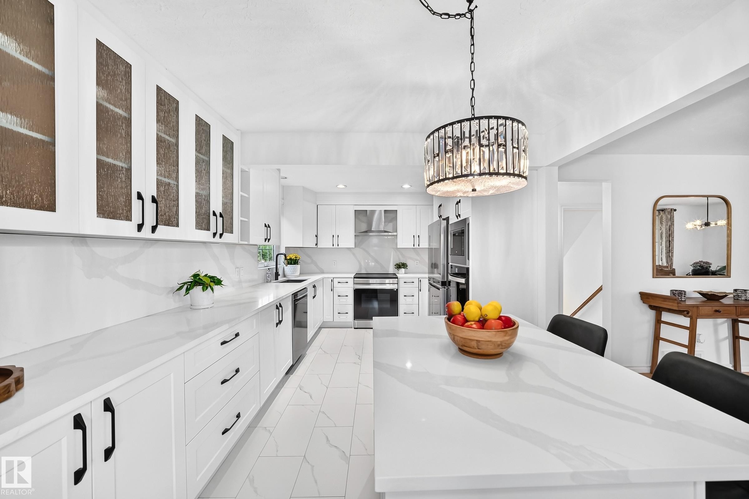 Bright kitchen featuring white cabinetry, a large center island with seating, integrated appliances, white countertops with a subtle gray pattern, and a decorative chandelier - 10323 138 Street Nw, Edmonton, AB - Indoor