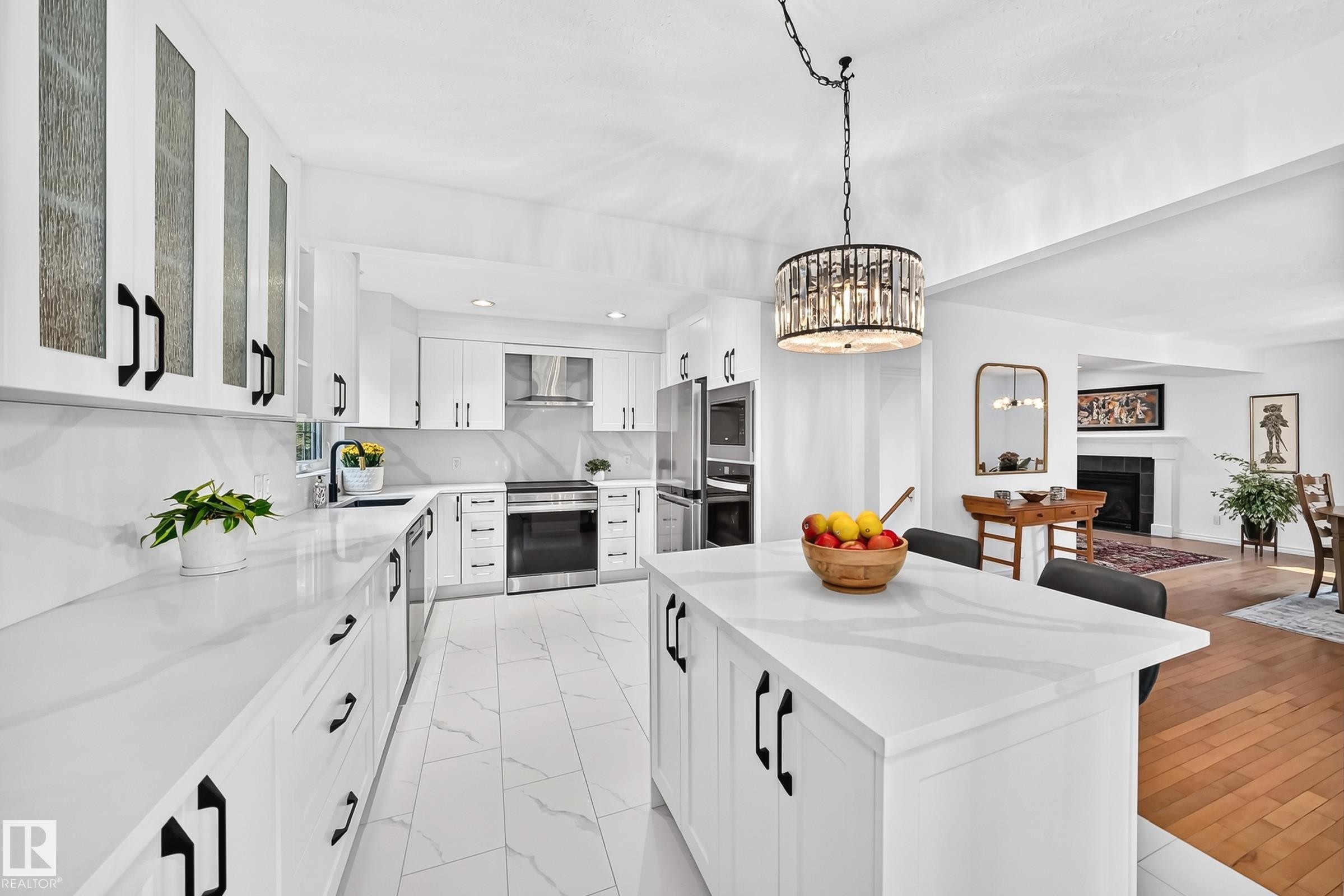 Contemporary kitchen featuring white cabinetry with black hardware, white countertops, tile flooring, and a central island with seating - 10323 138 Street Nw, Edmonton, AB - Indoor