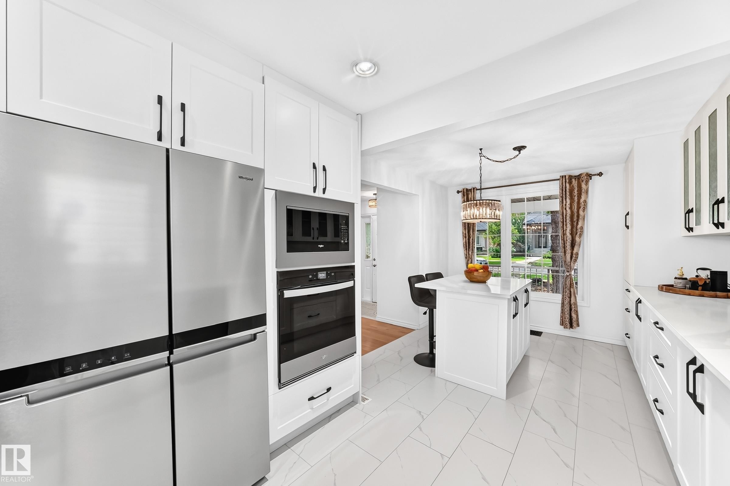 Modern kitchen featuring white shaker cabinetry with black hardware, stainless steel appliances, a center island with pendant lighting, and large format tile flooring - 10323 138 Street Nw, Edmonton, AB - Indoor Photo Showing Kitchen