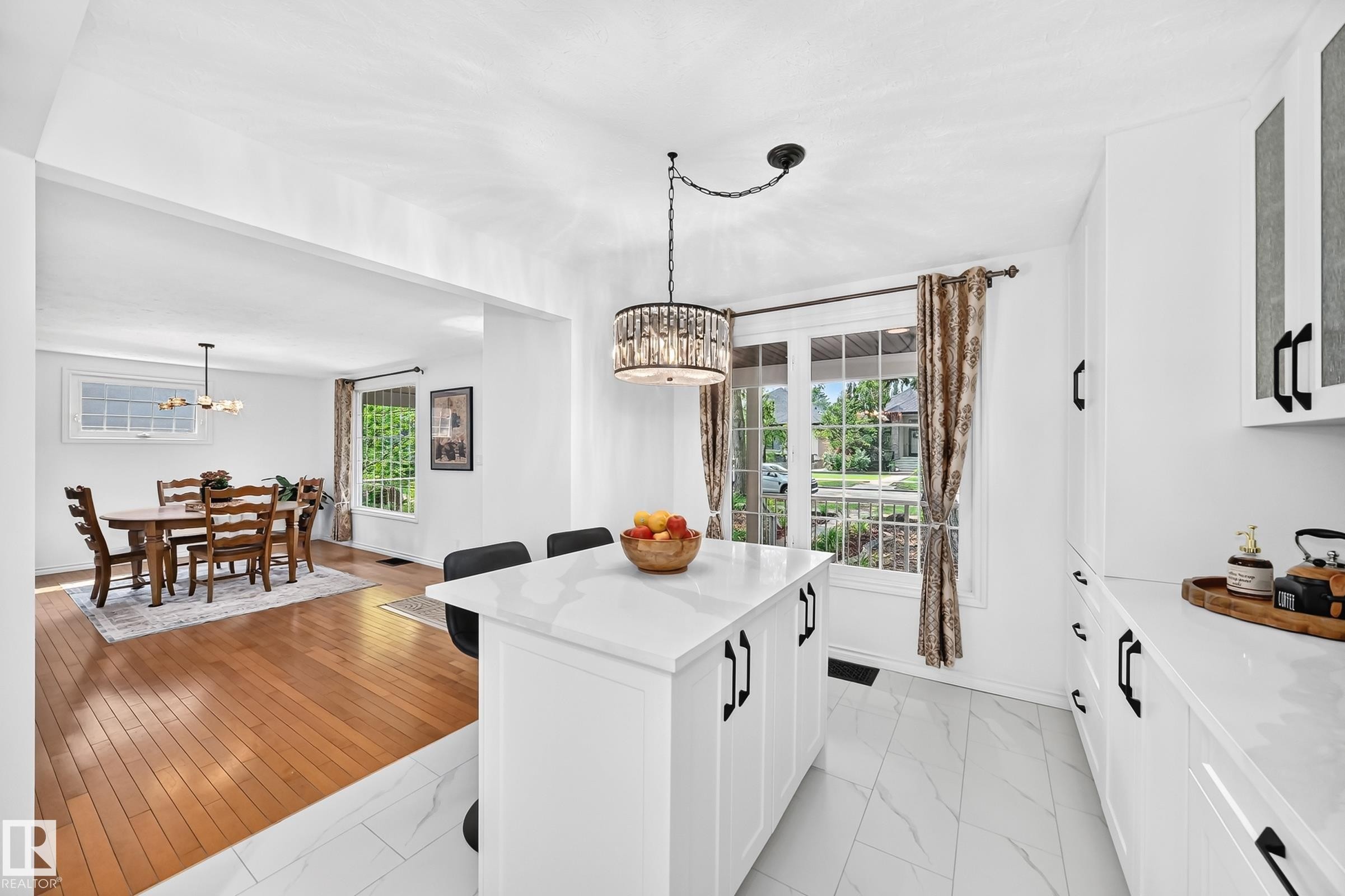 Kitchen featuring a central island with white countertop, white cabinetry with black hardware, and marble-look floor tiles - 10323 138 Street Nw, Edmonton, AB - Indoor