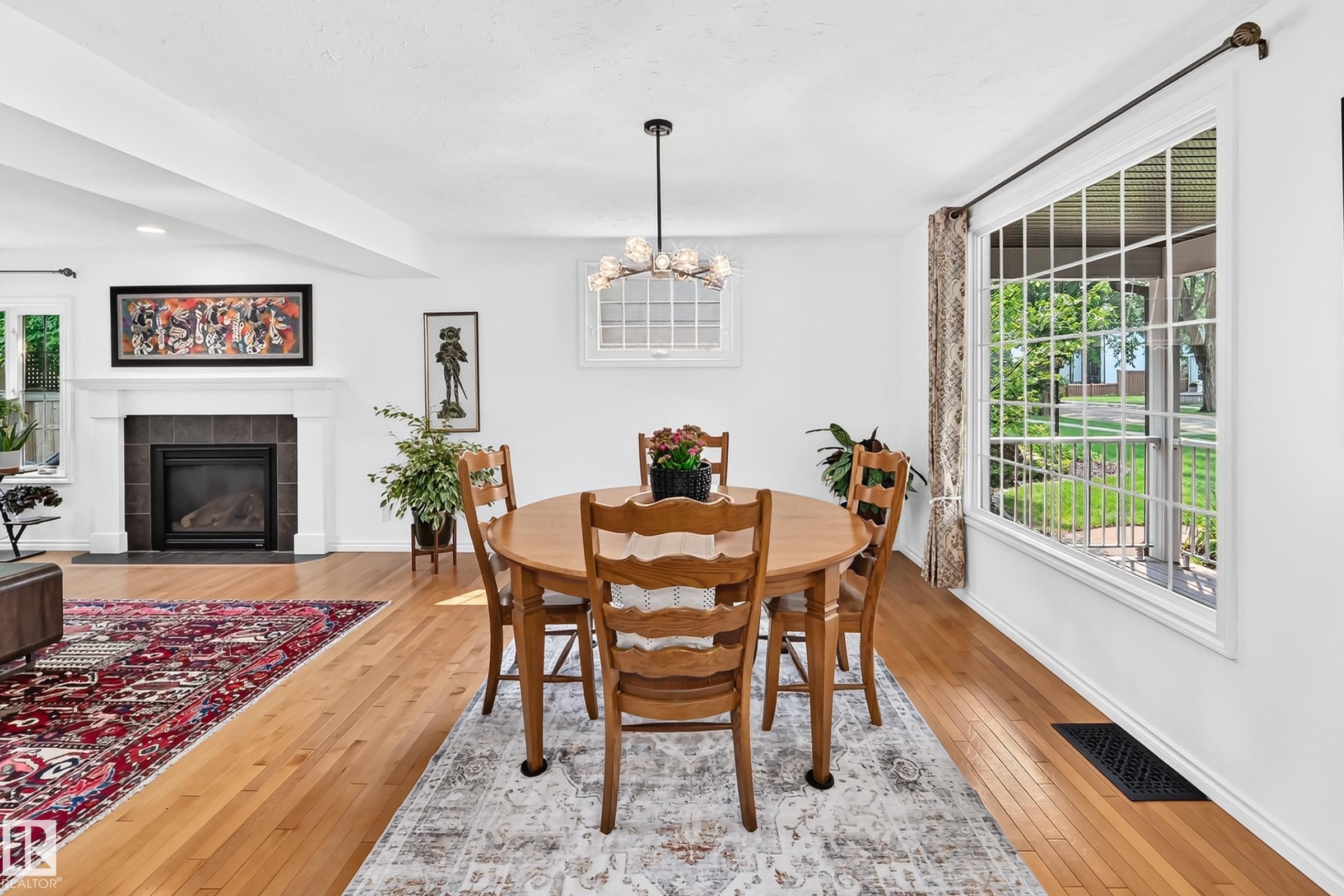 Hardwood flooring extends throughout this open-concept space, featuring a large picture window with grid detailing - 10323 138 Street Nw, Edmonton, AB - Indoor Photo Showing Other Room With Fireplace