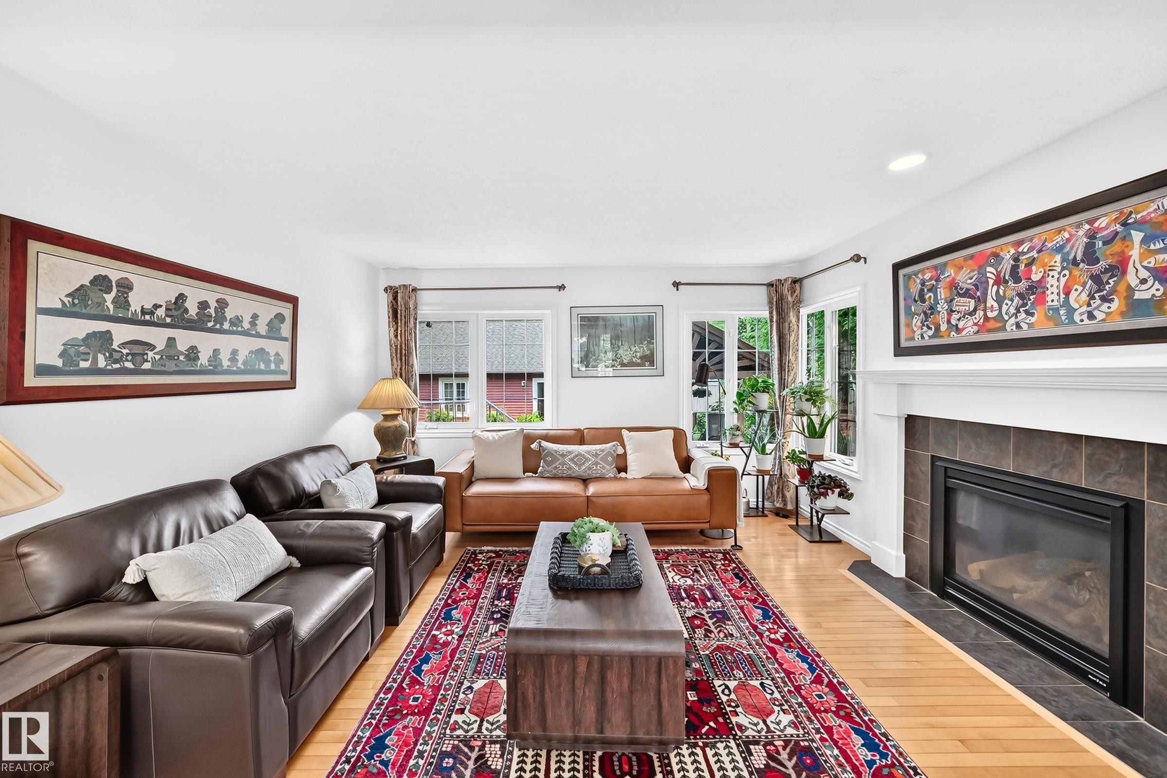 Living area featuring light wood-finish flooring, a contemporary fireplace with a dark tile surround and white mantel, and multiple windows - 10323 138 Street Nw, Edmonton, AB - Indoor Photo Showing Living Room With Fireplace