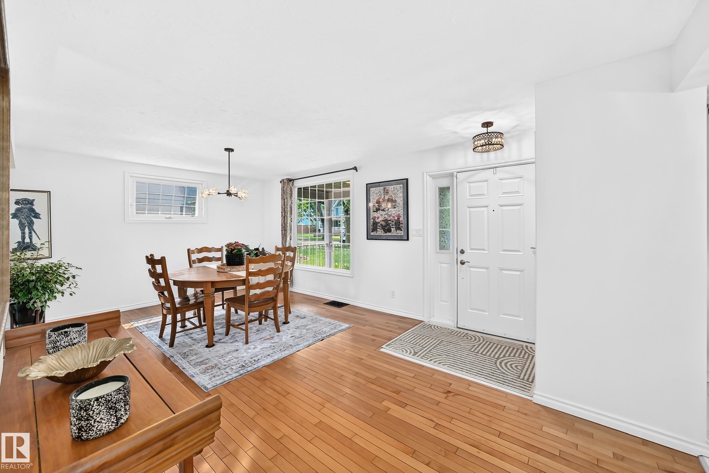 Open-concept entryway featuring wood-finish flooring, a white paneled front door with sidelight, and a decorative semi-flush mount light fixture - 10323 138 Street Nw, Edmonton, AB - Indoor