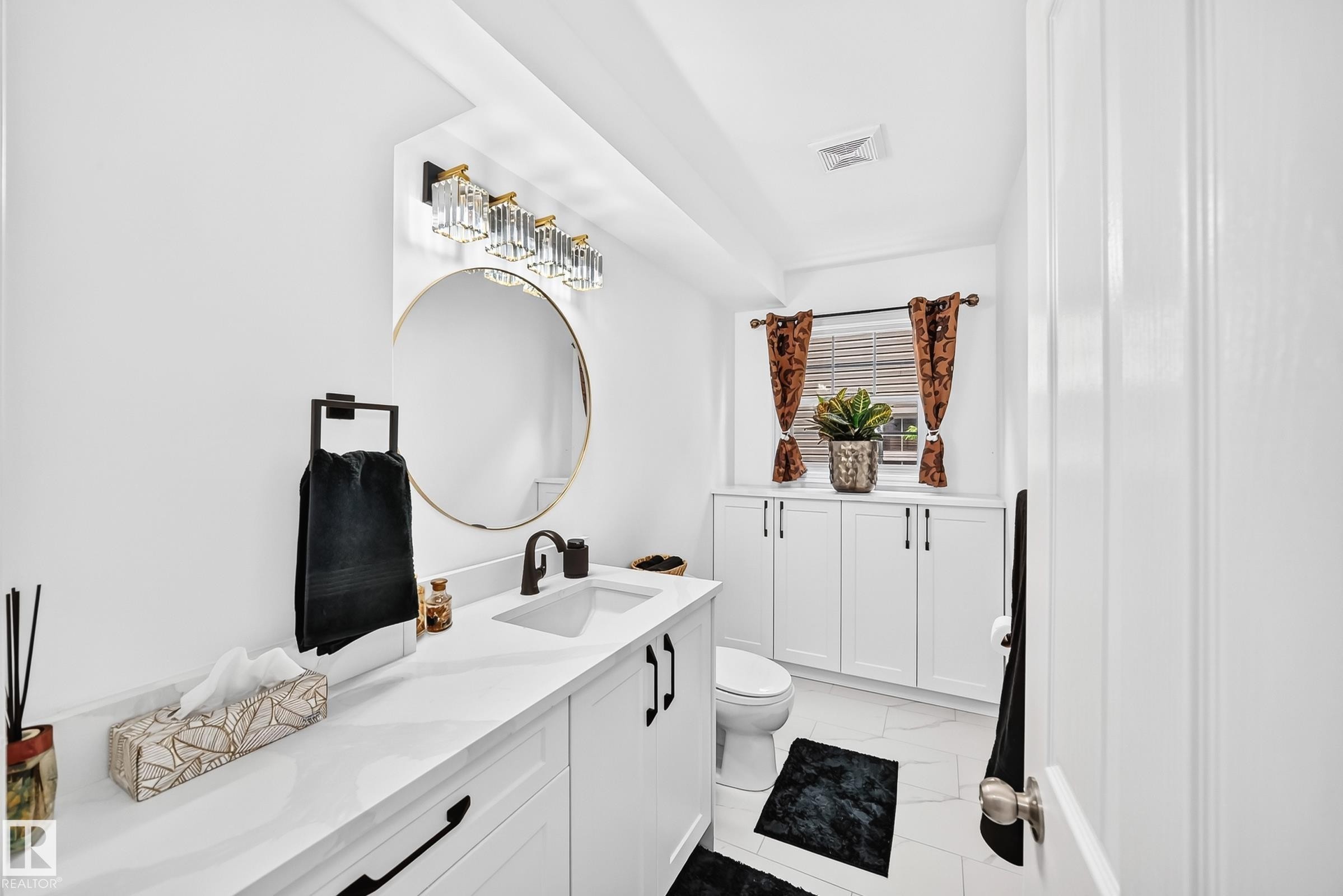 Bathroom featuring a white vanity with integrated sink, black hardware, and a round mirror - 10323 138 Street Nw, Edmonton, AB - Indoor Photo Showing Bathroom
