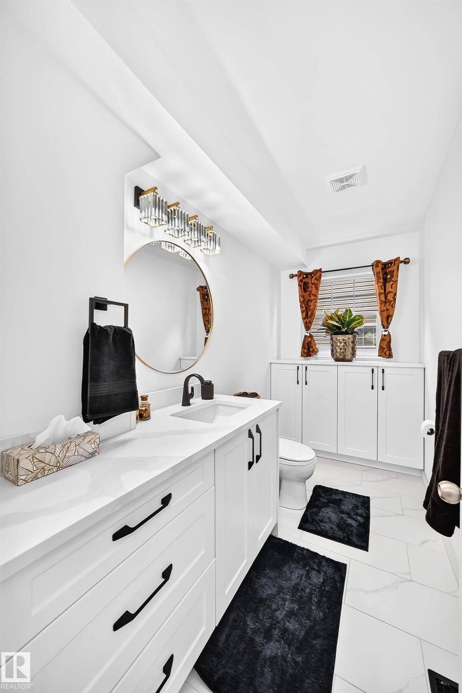 Bathroom featuring a white vanity with an integrated sink, matte black hardware, and a round gold-framed mirror - 10323 138 Street Nw, Edmonton, AB - Indoor Photo Showing Bathroom