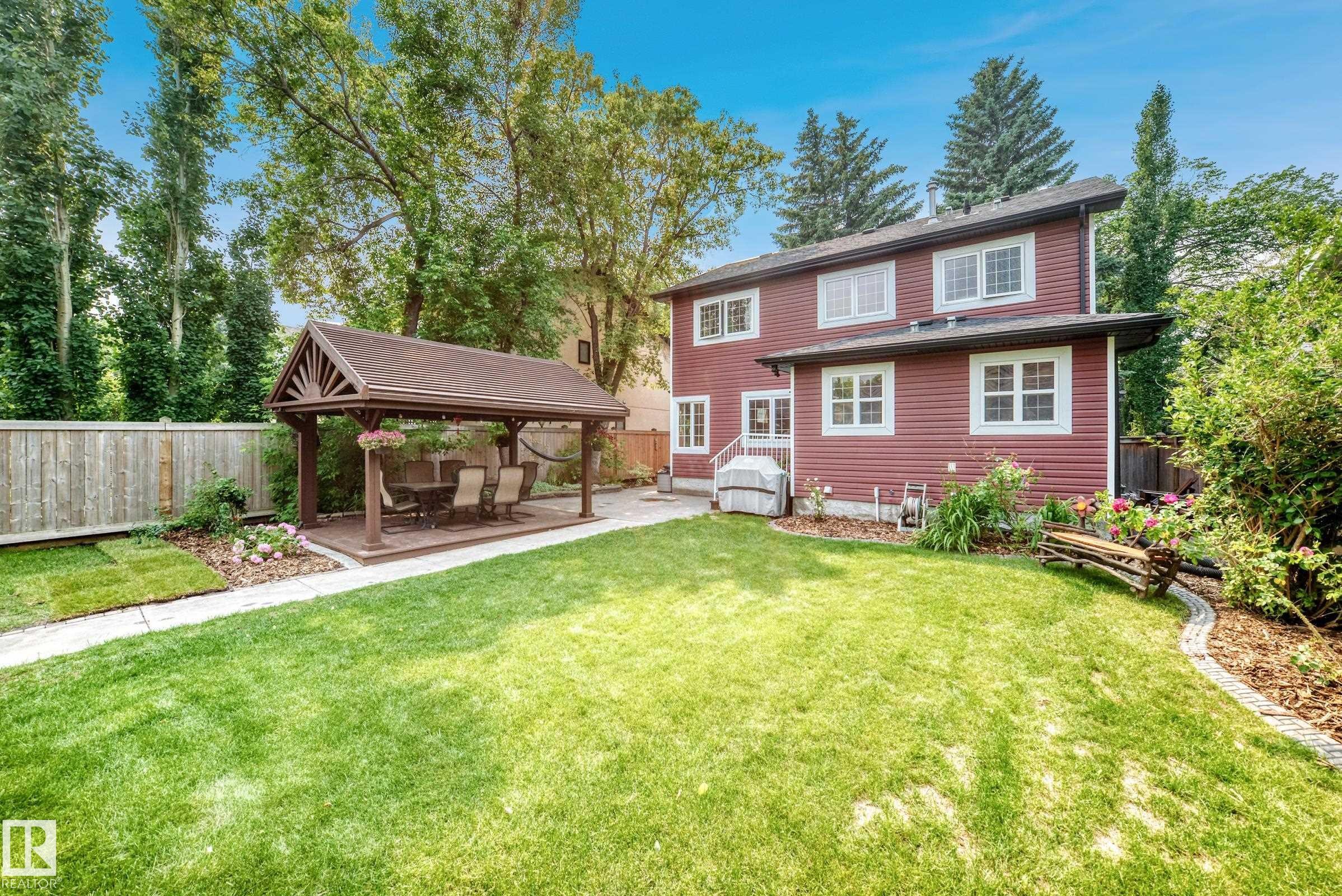 Expansive backyard featuring a large lawn, a paved patio, and a built-in gazebo with a shingled roof - 10323 138 Street Nw, Edmonton, AB - Outdoor With Deck Patio Veranda