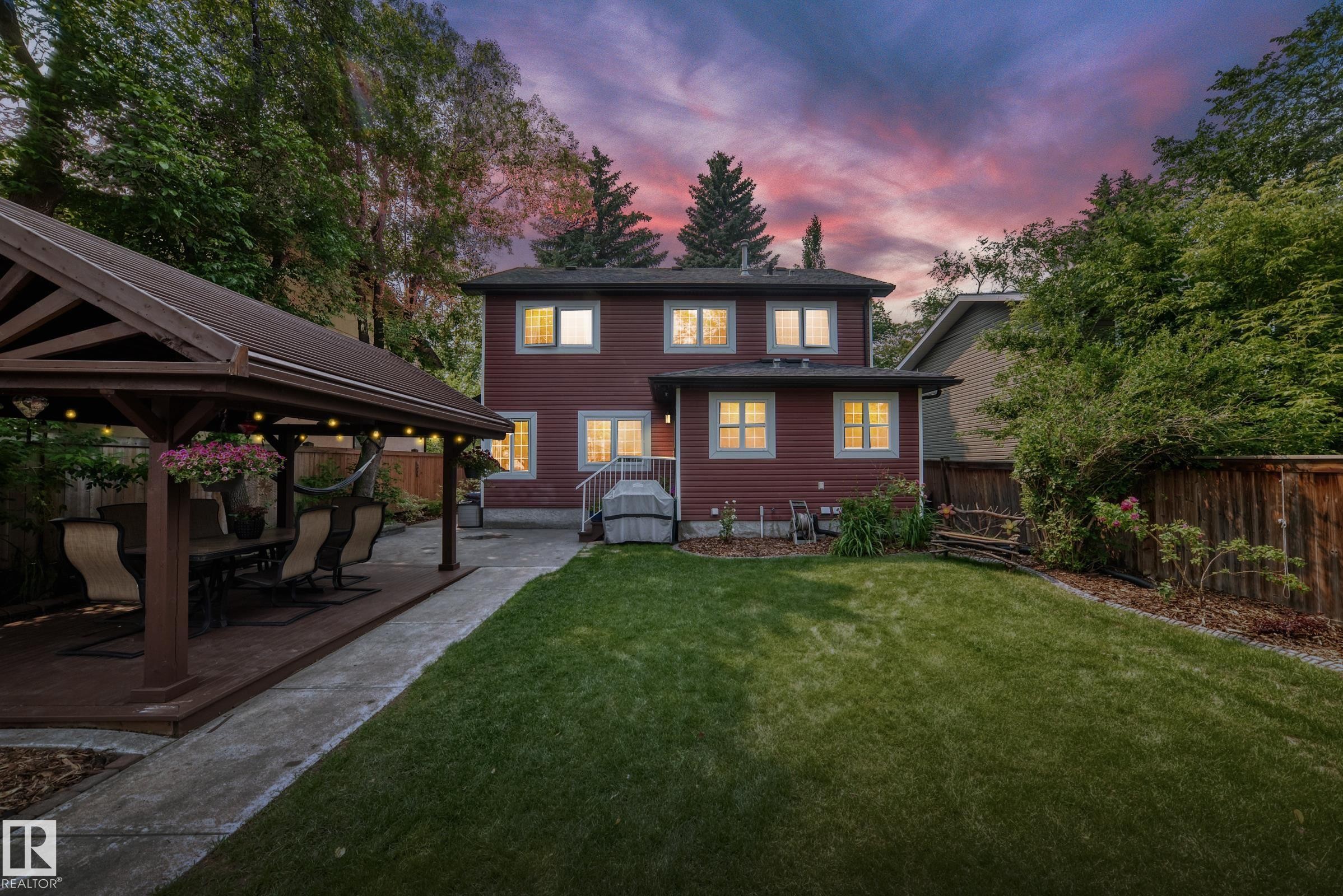 Expansive backyard featuring a manicured lawn, a covered gazebo with a wood deck, a concrete walkway, and a red-sided two-story residence with multiple windows - 10323 138 Street Nw, Edmonton, AB - Outdoor
