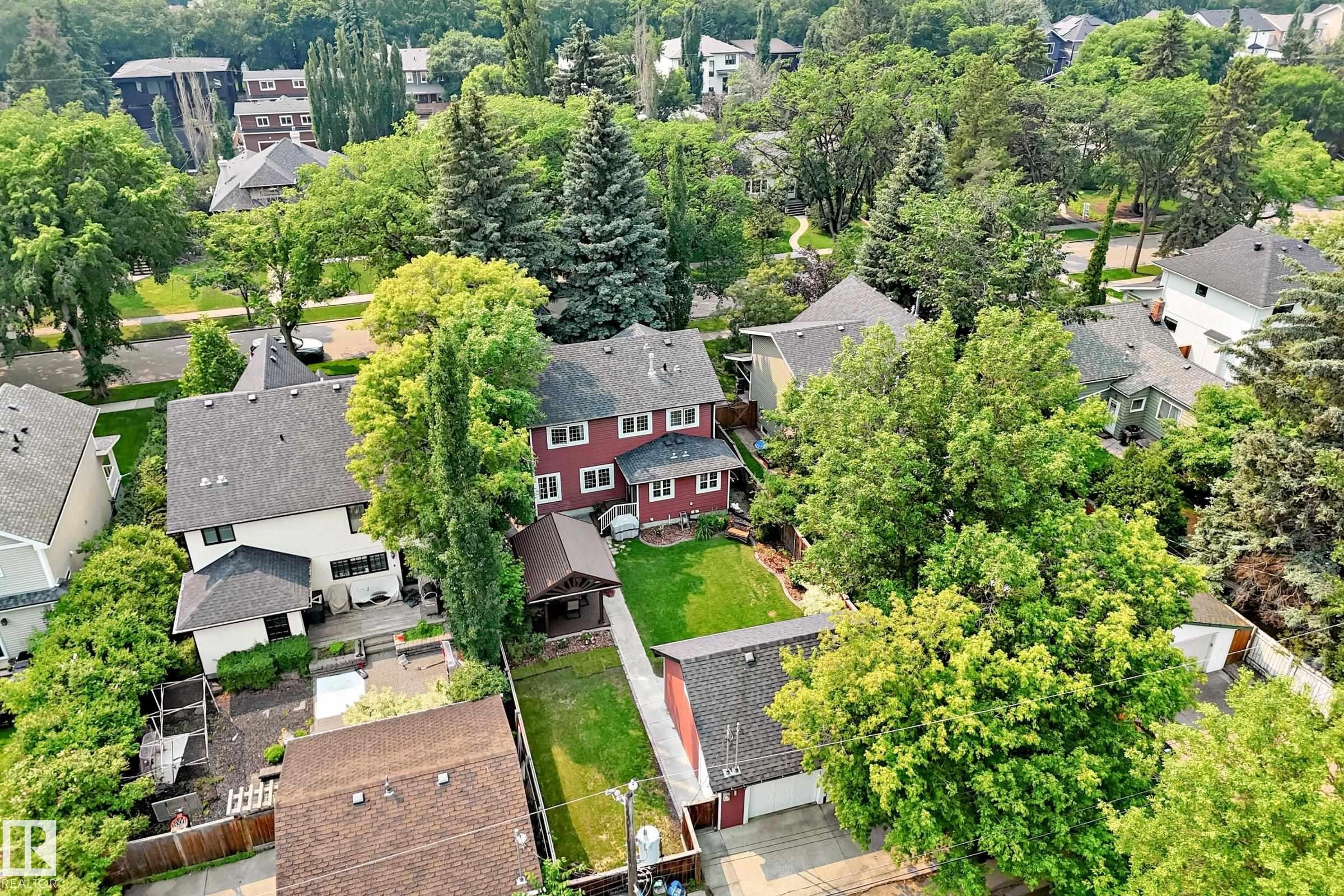 Red exterior residence with a contrasting roof, featuring a substantial backyard lawn and mature trees - 10323 138 Street Nw, Edmonton, AB - Outdoor
