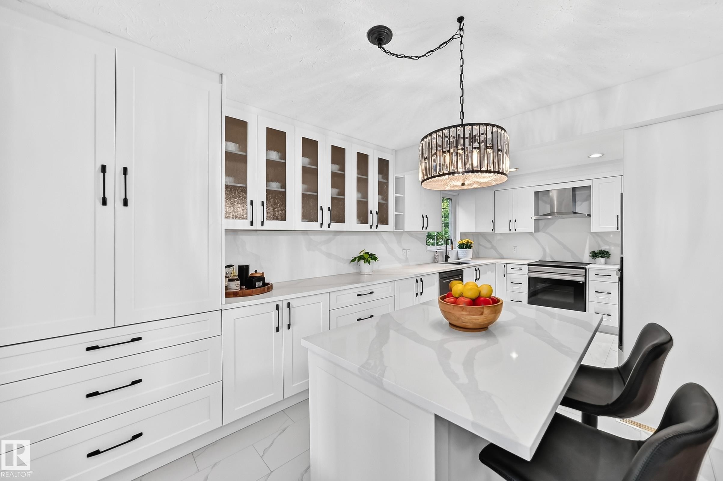 Bright kitchen featuring white cabinetry with black hardware, a center island with a stone-finish countertop, matching stone-finish backsplash, and a contemporary chandelier - 10323 138 Street Nw, Edmonton, AB - Indoor