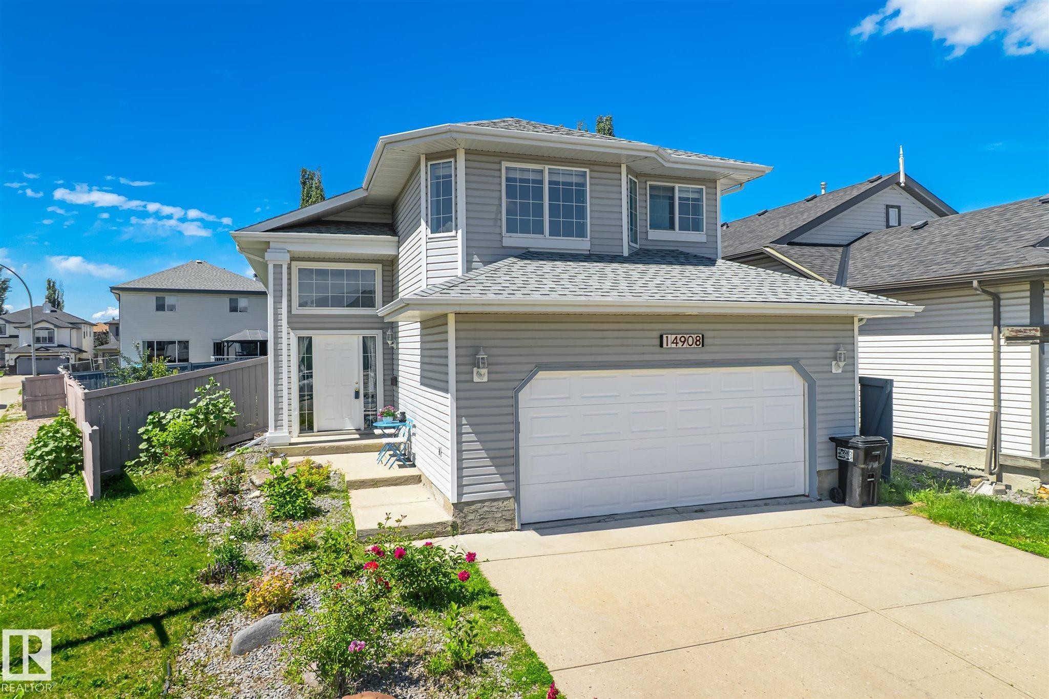Two-story residence featuring light gray siding, a prominent two-car garage with a concrete driveway, and a welcoming front entrance with a white door - 14908 137 Street Nw, Edmonton, AB - Outdoor