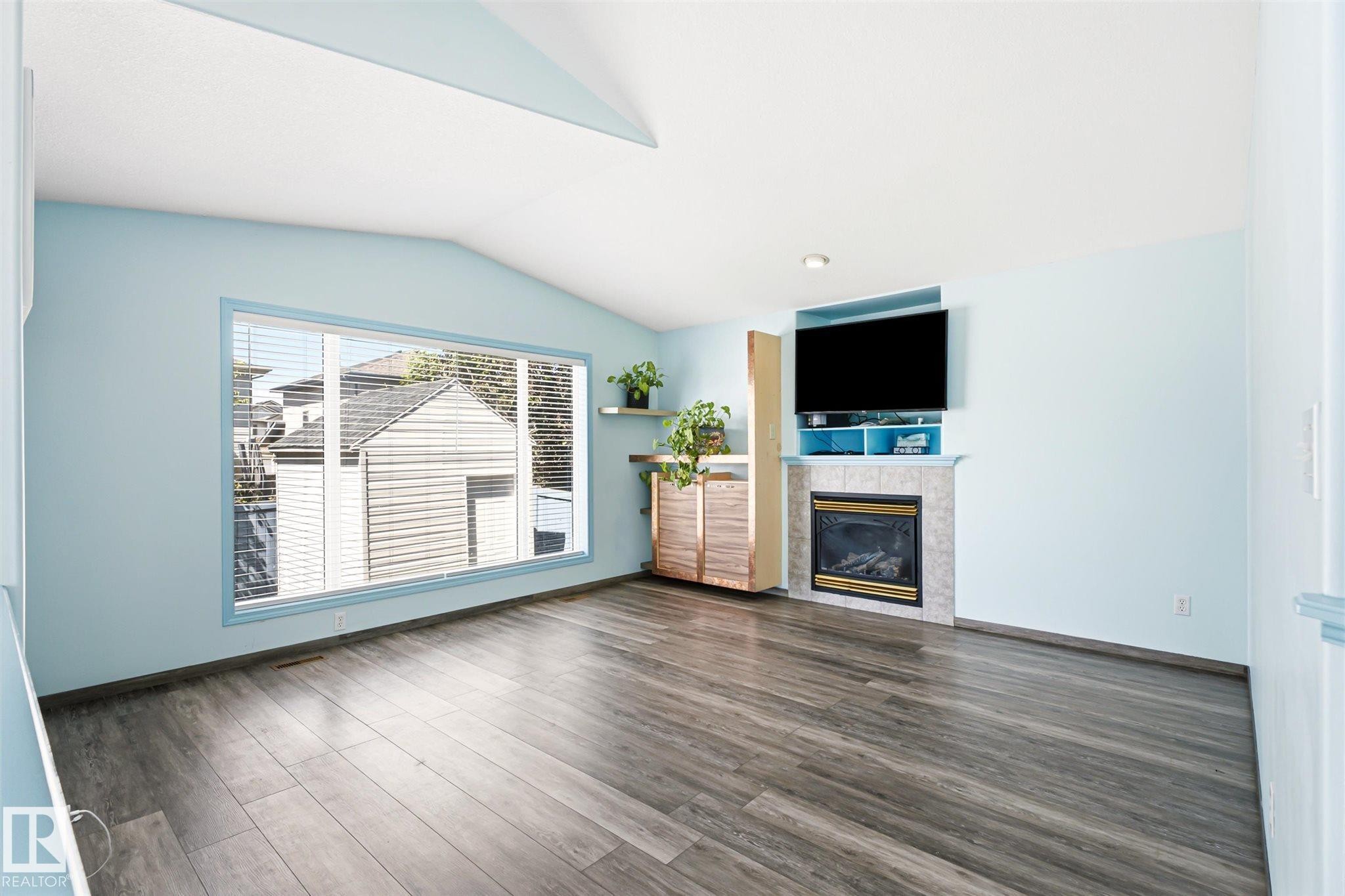 Spacious living area featuring wood-finish flooring, a large picture window, and a vaulted ceiling - 14908 137 Street Nw, Edmonton, AB - Indoor Photo Showing Living Room With Fireplace