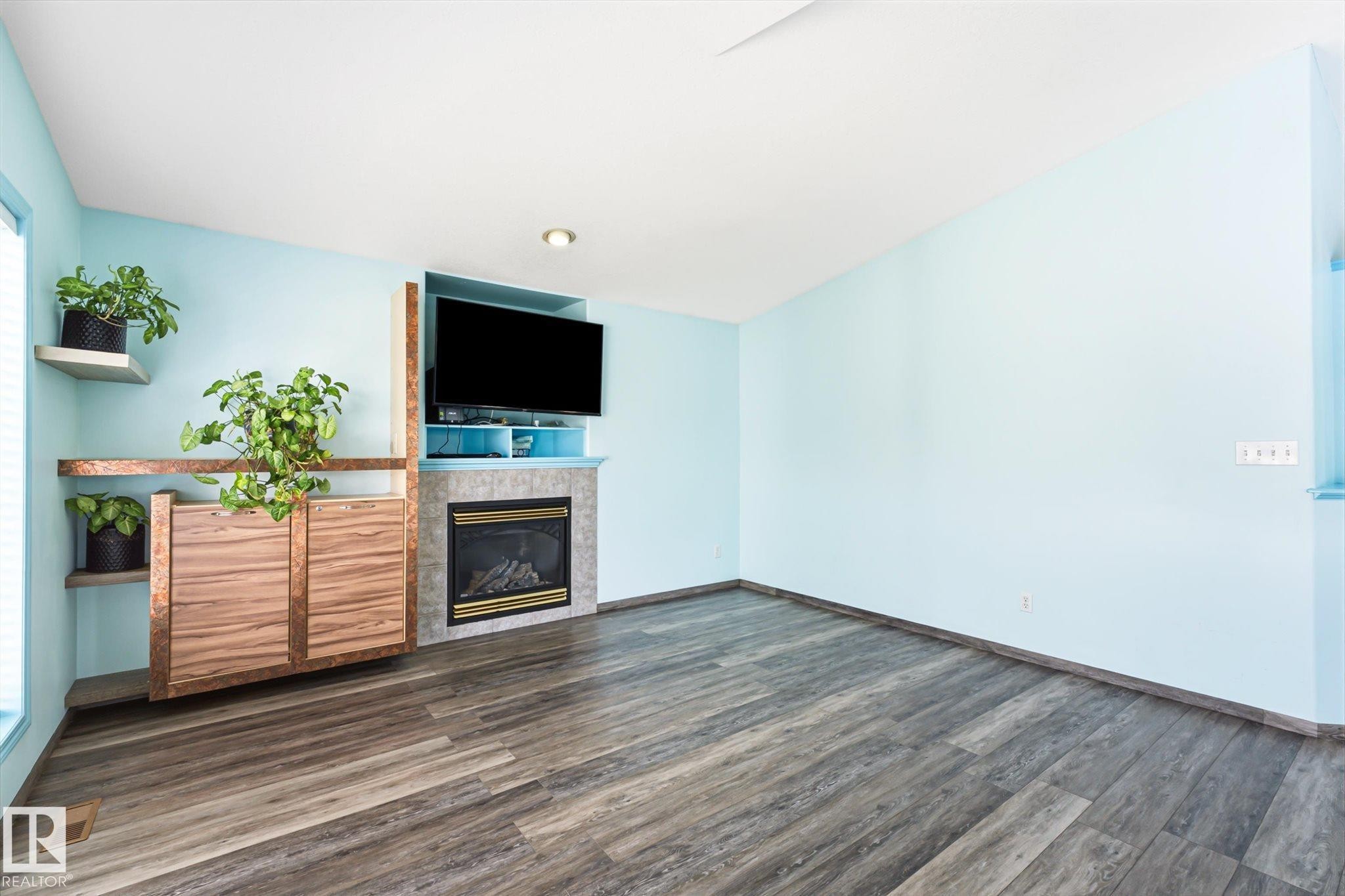 Living area featuring wood-finish flooring, a built-in fireplace with a stone surround, and integrated shelving with cabinetry - 14908 137 Street Nw, Edmonton, AB - Indoor With Fireplace