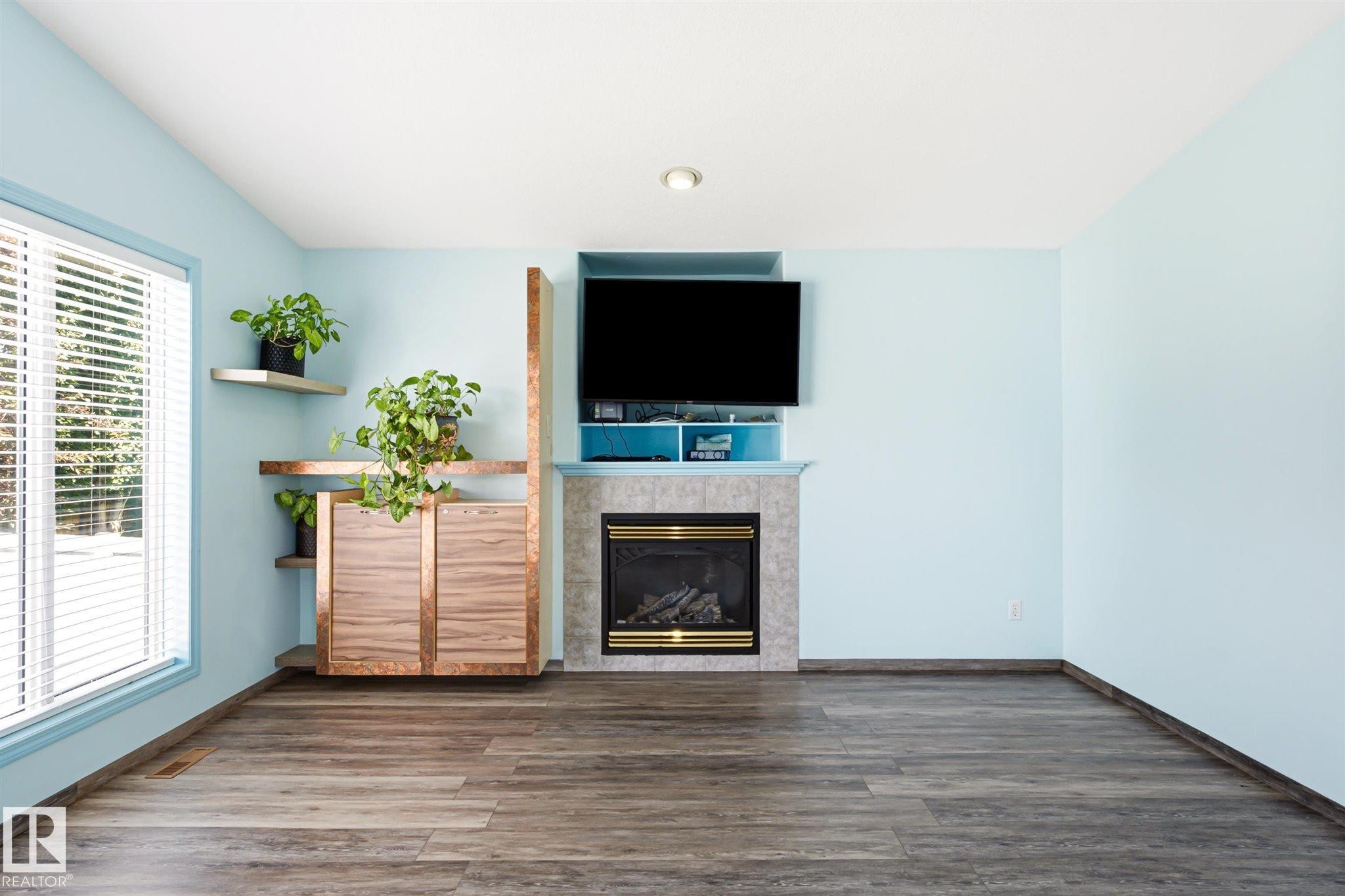 Living space featuring wood-finish flooring and a corner window with blinds - 14908 137 Street Nw, Edmonton, AB - Indoor With Fireplace