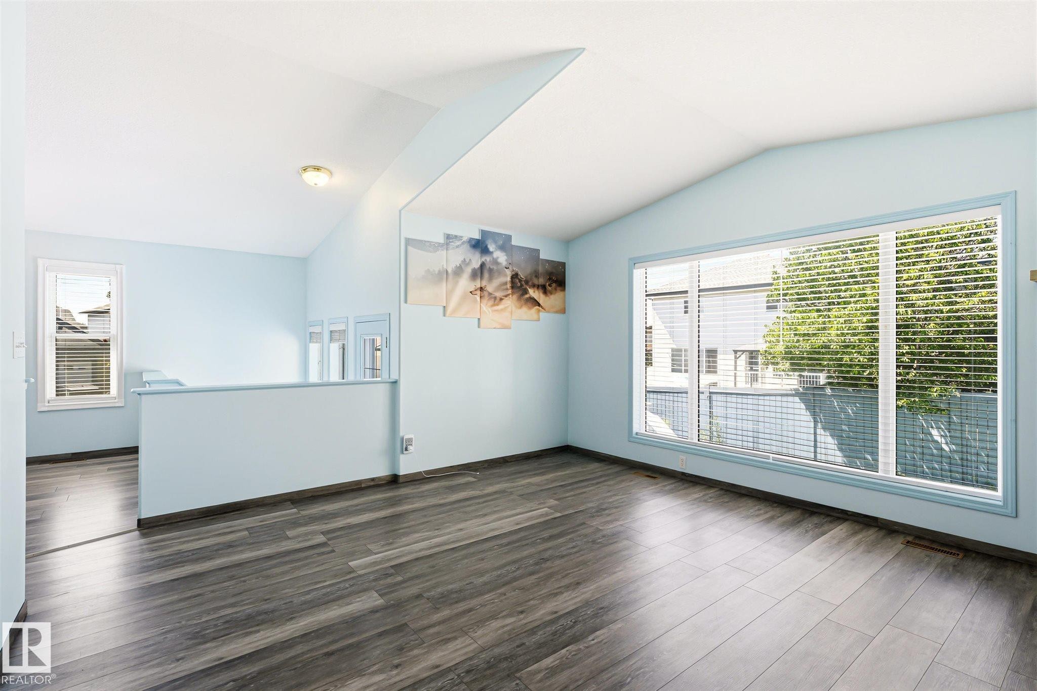 Spacious room featuring vaulted ceilings, wood-finish flooring, a large multi-pane window, and a half-wall partition - 14908 137 Street Nw, Edmonton, AB - Indoor Photo Showing Other Room