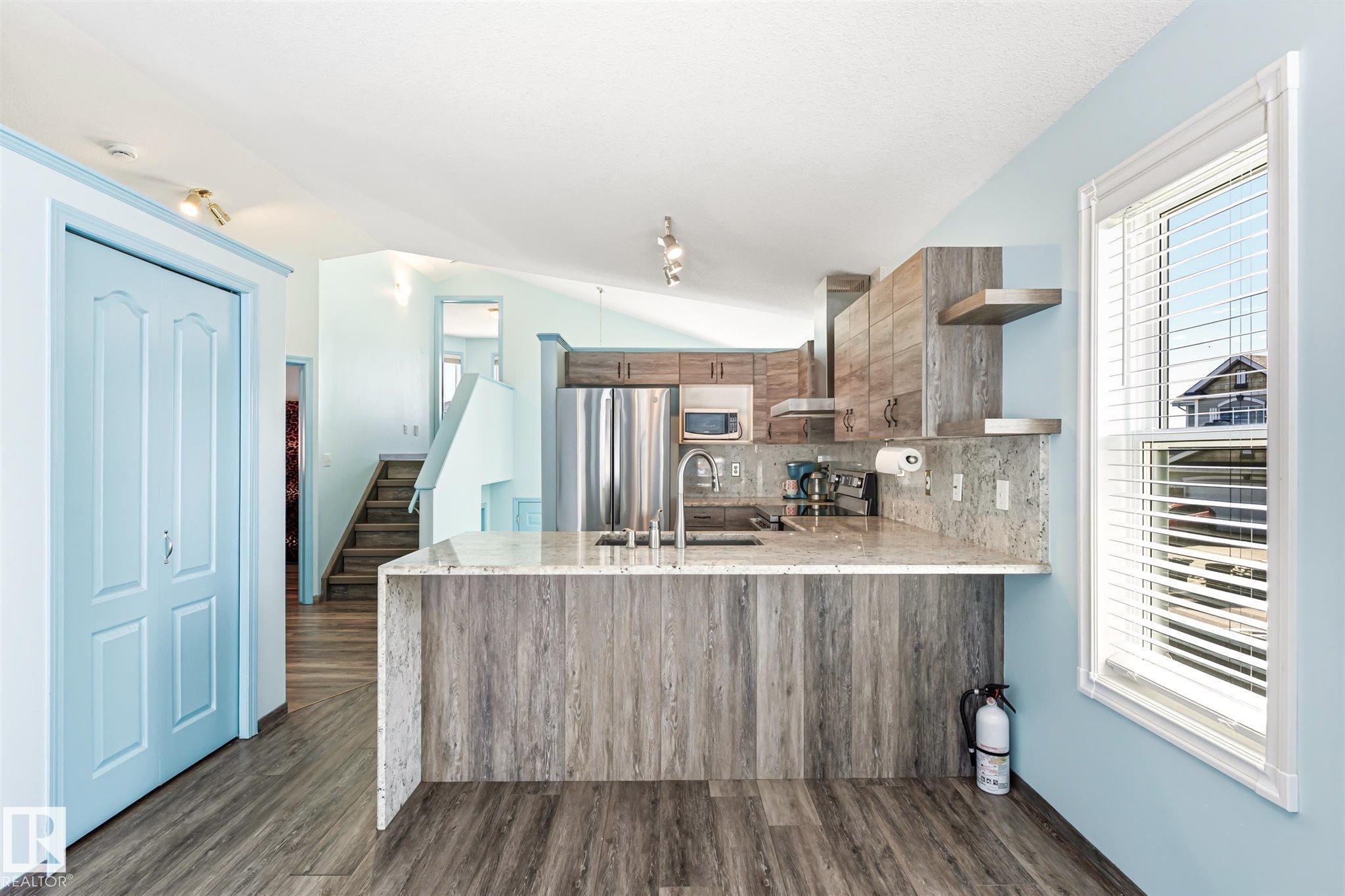 Contemporary kitchen featuring wood-finish cabinetry, stainless steel appliances, and a stone countertop with matching backsplash - 14908 137 Street Nw, Edmonton, AB - Indoor Photo Showing Kitchen