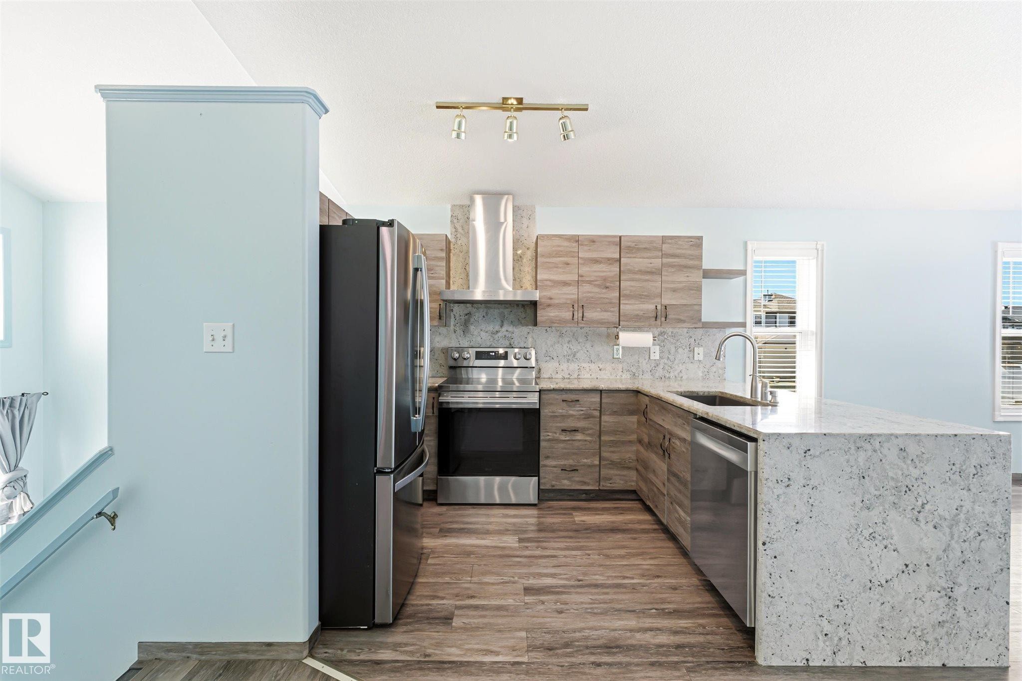 Modern kitchen with light wood-finish cabinetry, stainless steel appliances, and a large central island featuring a light-toned stone countertop - 14908 137 Street Nw, Edmonton, AB - Indoor Photo Showing Kitchen With Stainless Steel Kitchen