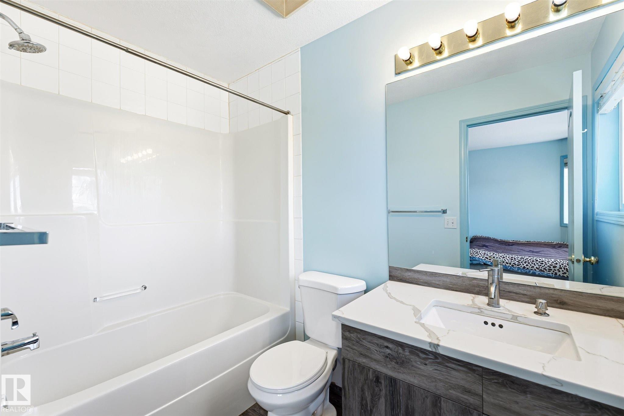 Bathroom featuring a white bathtub and shower surround, a toilet, a vanity with a white countertop and integrated sink, a large mirror, and overhead lighting - 14908 137 Street Nw, Edmonton, AB - Indoor Photo Showing Bathroom