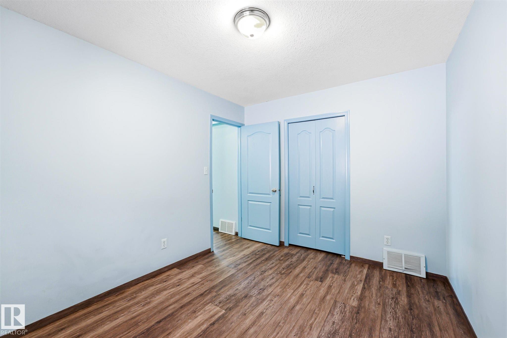 Interior room with wood-finish flooring, light blue walls, and a ceiling-mounted light fixture - 14908 137 Street Nw, Edmonton, AB - Indoor Photo Showing Other Room