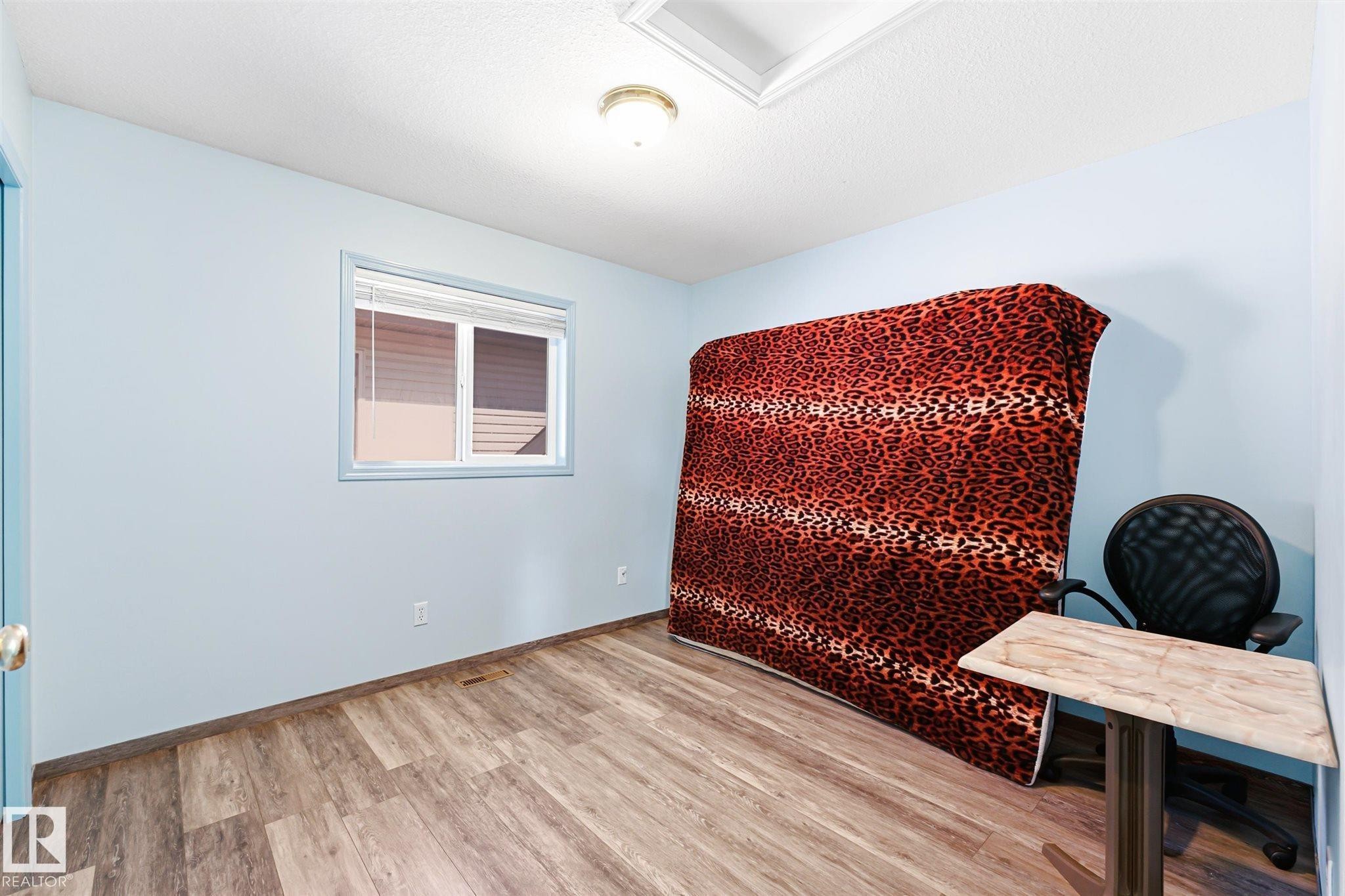 Room featuring wood-finish flooring, light blue wall paint, and a window with blinds - 14908 137 Street Nw, Edmonton, AB - Indoor