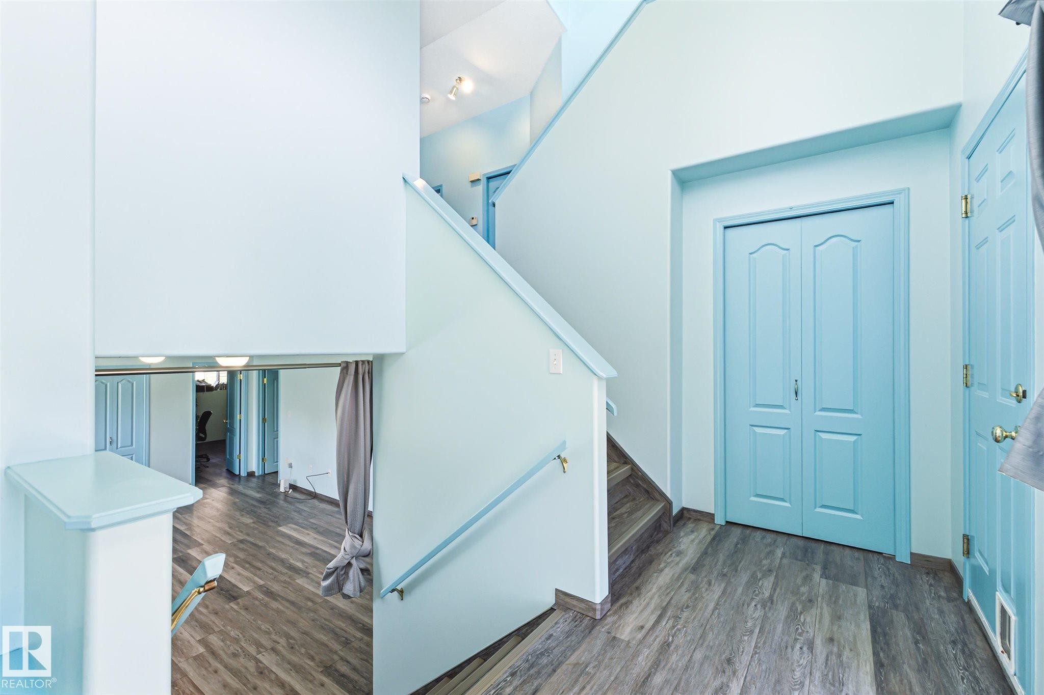 Multi-level interior featuring wood-finish flooring, light blue walls, and a staircase with a matching handrail - 14908 137 Street Nw, Edmonton, AB - Indoor Photo Showing Other Room