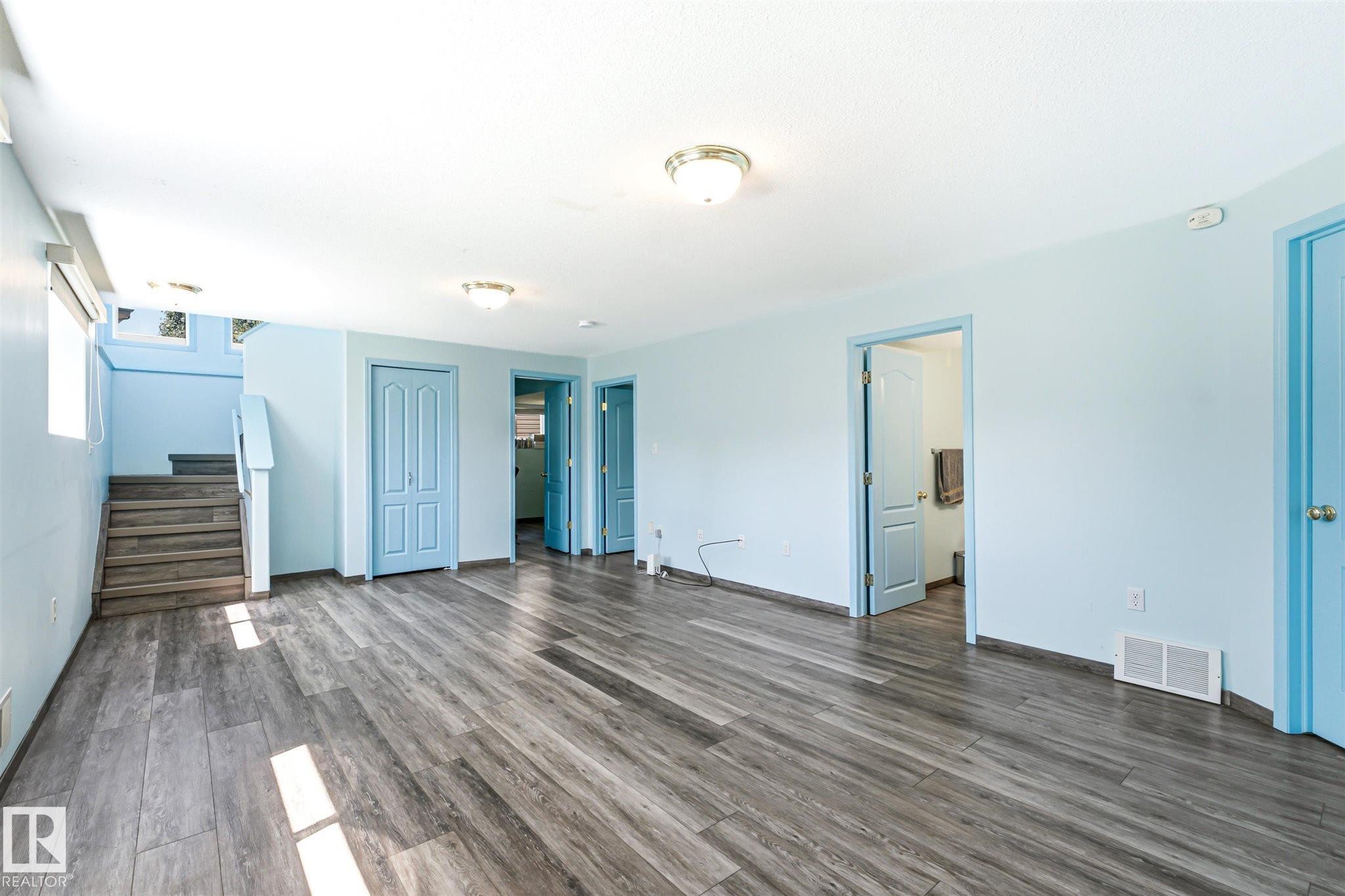 Spacious interior featuring wood-finish flooring, light blue painted walls, multiple light blue doors, and ceiling-mounted light fixtures - 14908 137 Street Nw, Edmonton, AB - Indoor Photo Showing Other Room