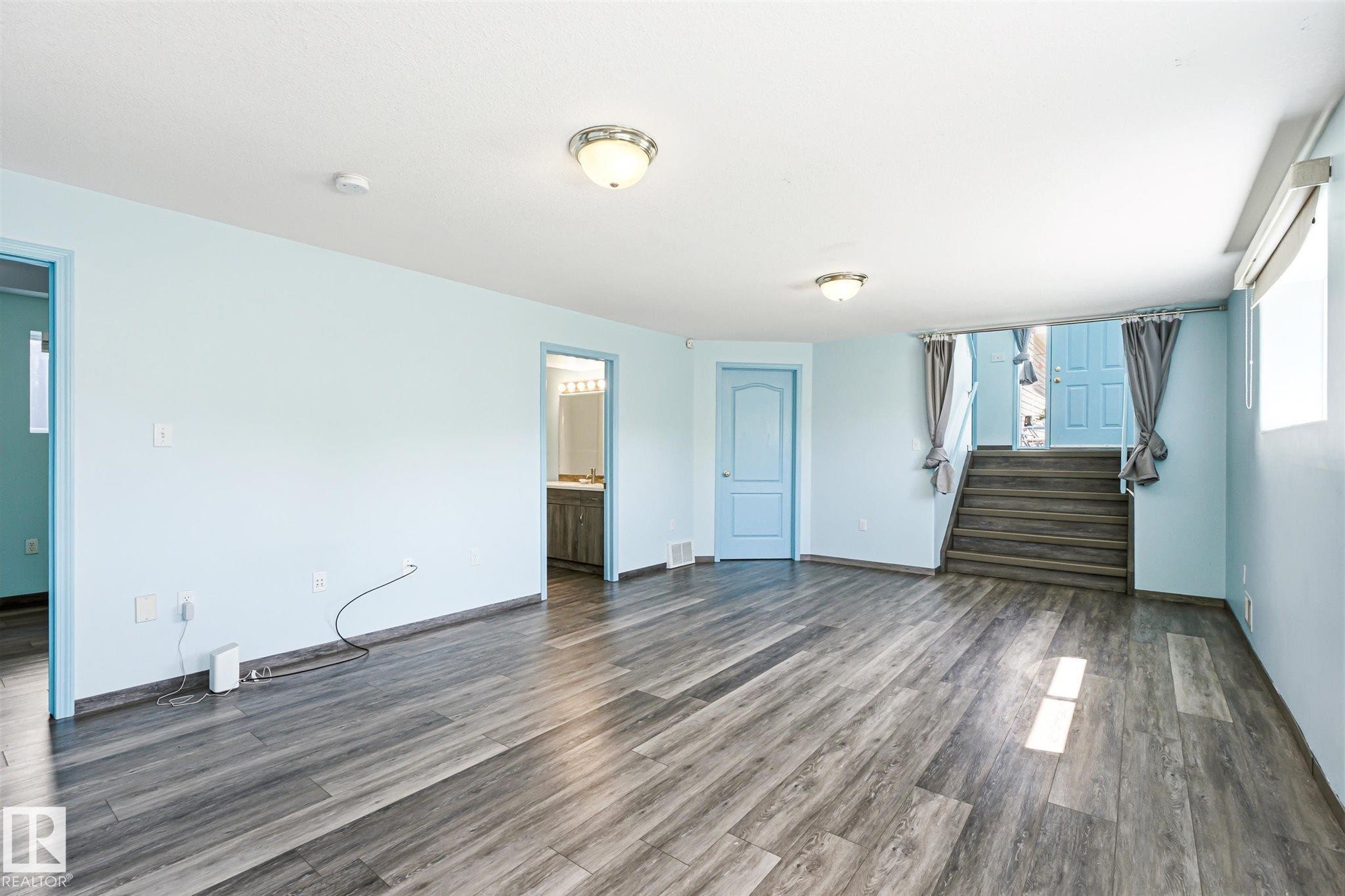 Spacious room featuring wood-finish flooring, light blue walls, and a white ceiling with flush-mount lighting fixtures - 14908 137 Street Nw, Edmonton, AB - Indoor Photo Showing Other Room